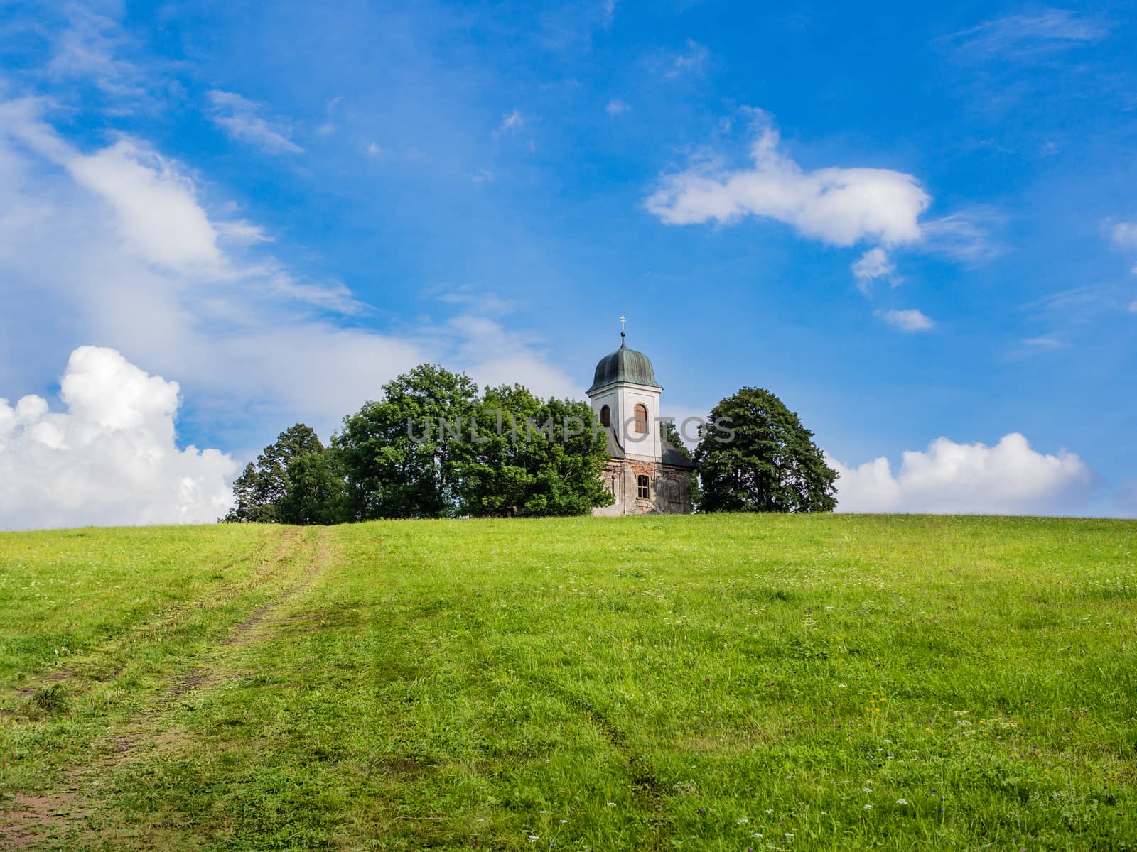 Christian church or chapel with white tower on top of the hill in the forest, horizon between green ground and blue cloudy sky, copy space, relaxing travelling under blue sky