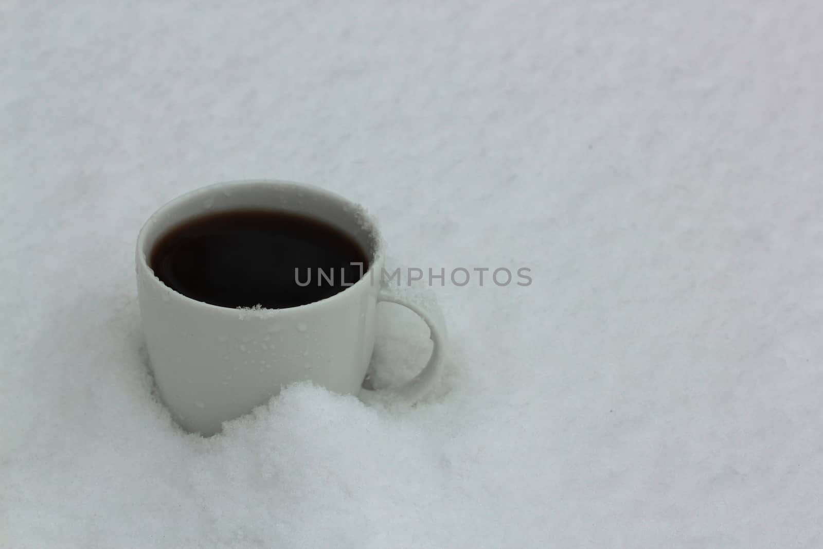 white cup of hot black coffee in snow