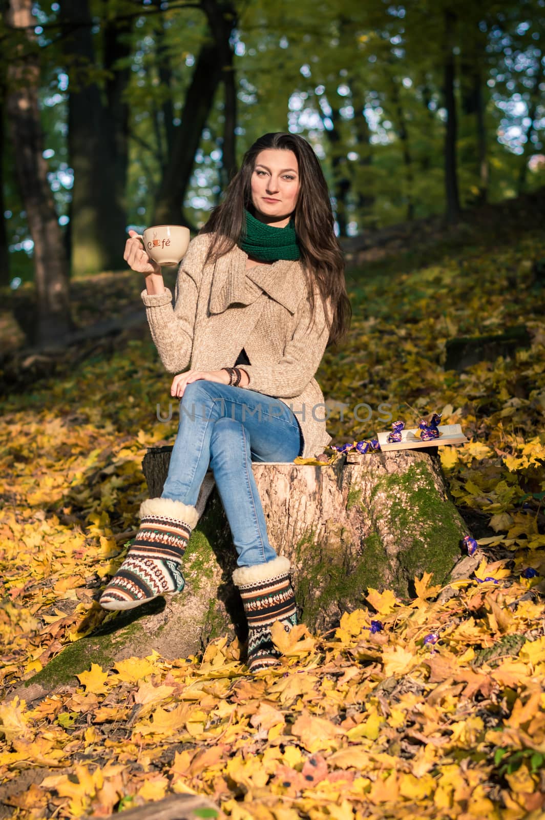 girl with a cup of coffee sitting on a tree stump in autumn Park