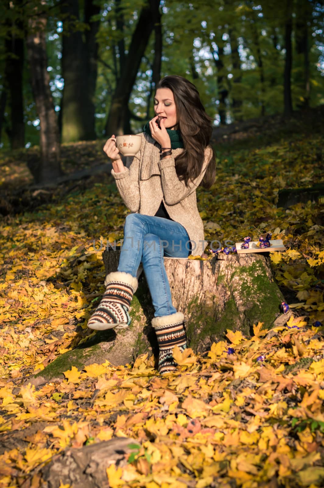 girl with a cup of coffee sitting on a tree stump in autumn Park