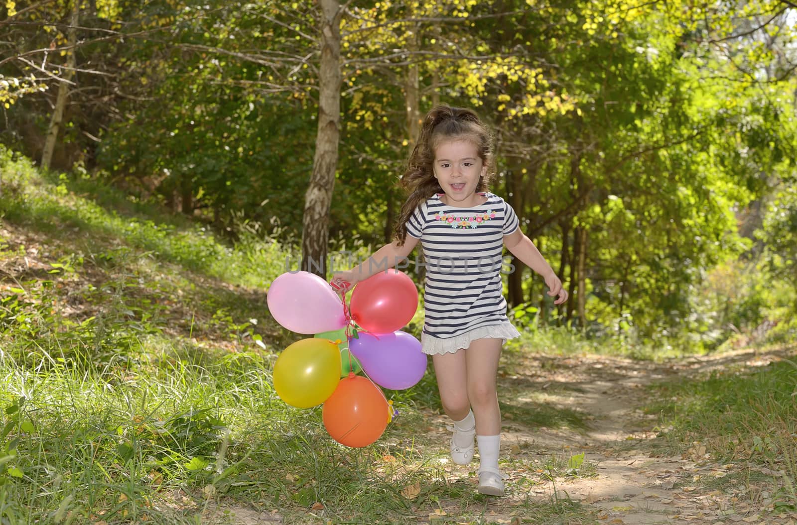 Little girl with colorful balloons in forest