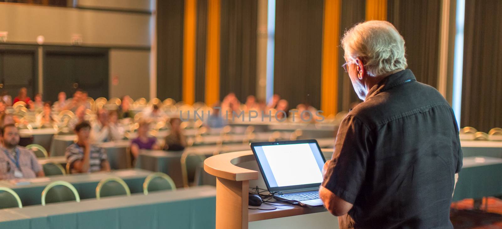 Casualy dressed senior professor giving talk at scientific conference. Audience at the conference hall. Research experts and entrepreneurship event.