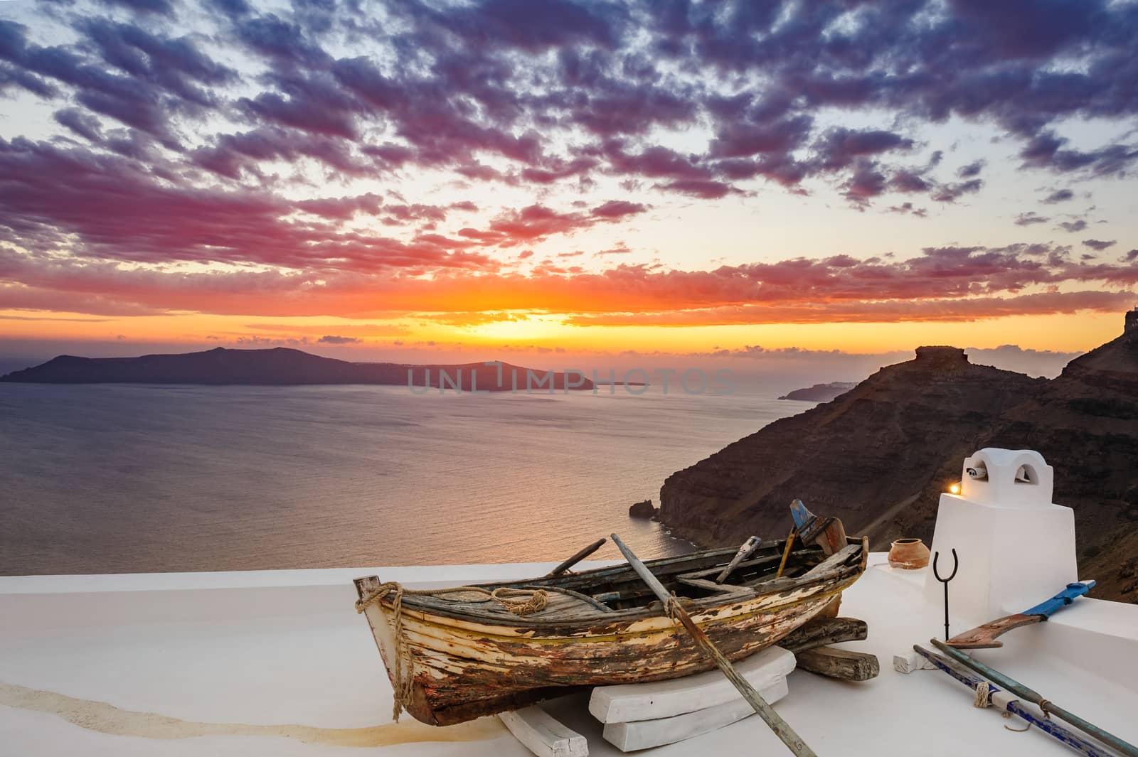 Old wooden fishermans''s boat on roofof house in Firostefani village with typical white architecture, Santorini island, Greece, during sunset over sea.