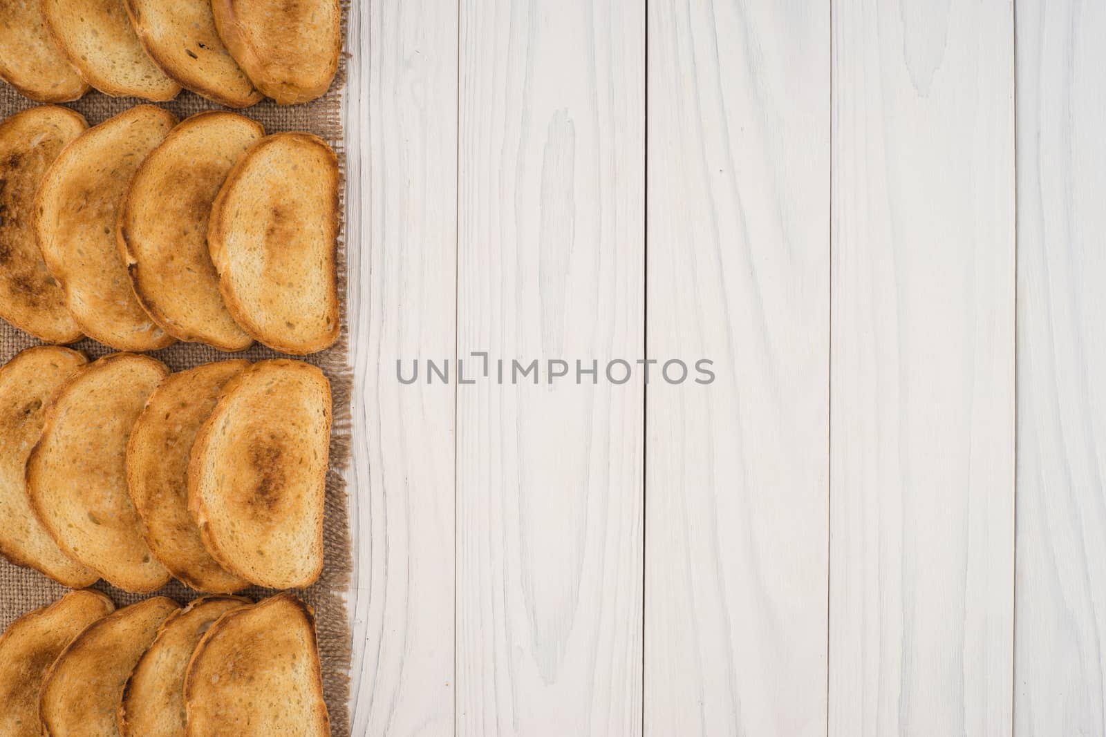Toasted bread on burlap and a white wooden table. Top view.