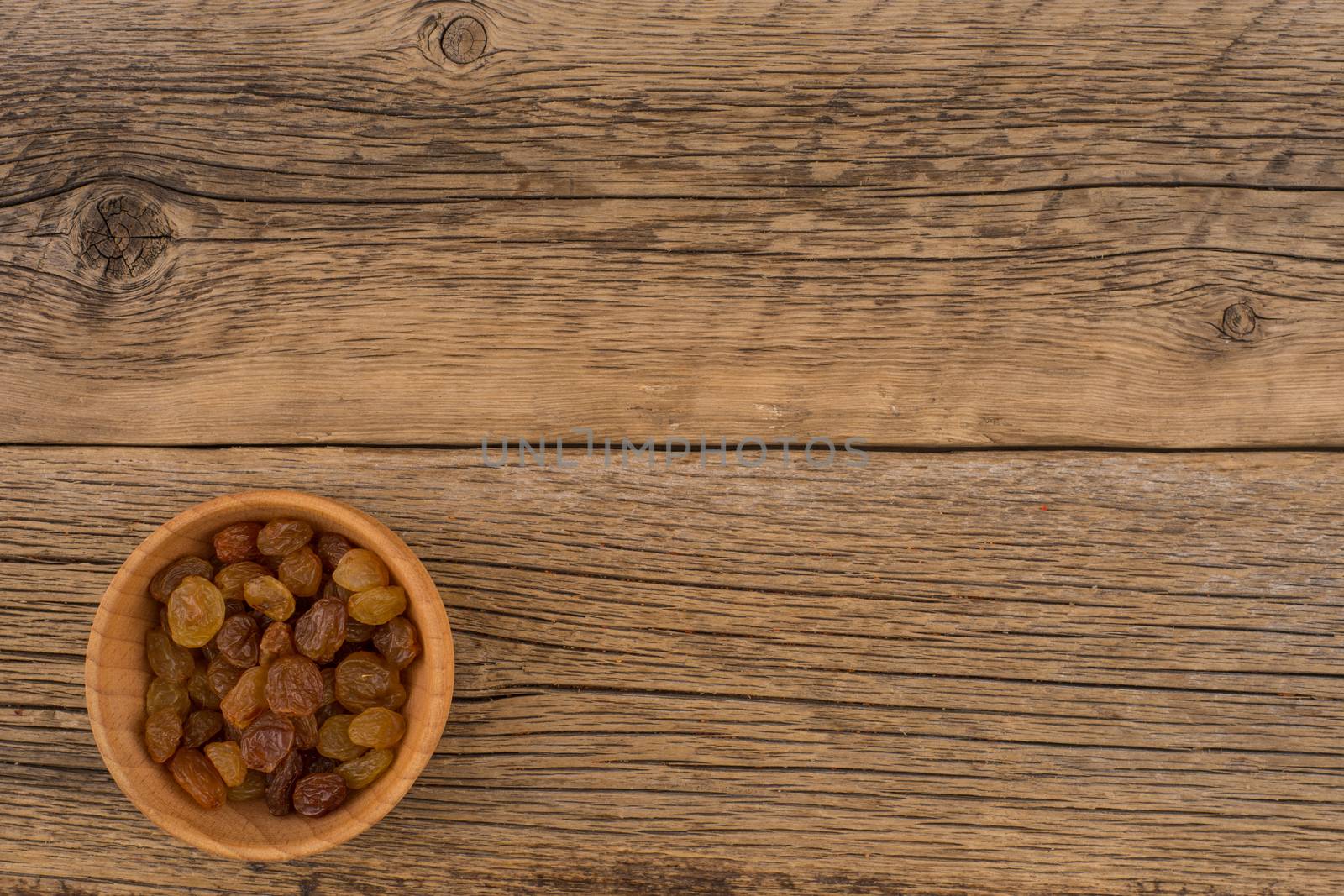 Raisins in a wooden bowl on the old wooden table. by DGolbay