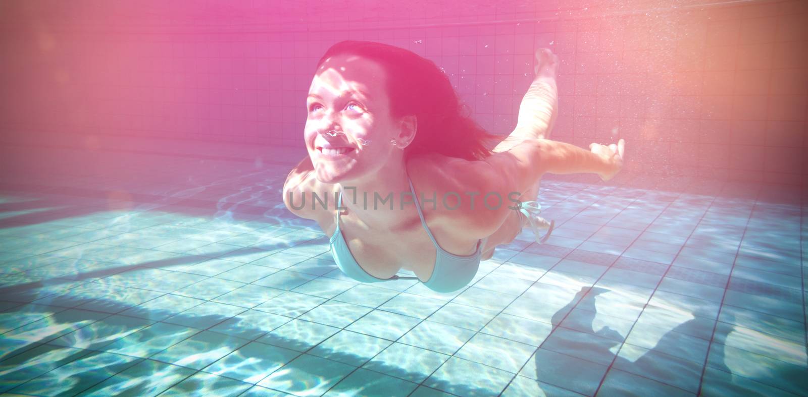 Pretty brunette smiling and swimming underwater in the swimming pool at the leisure centre