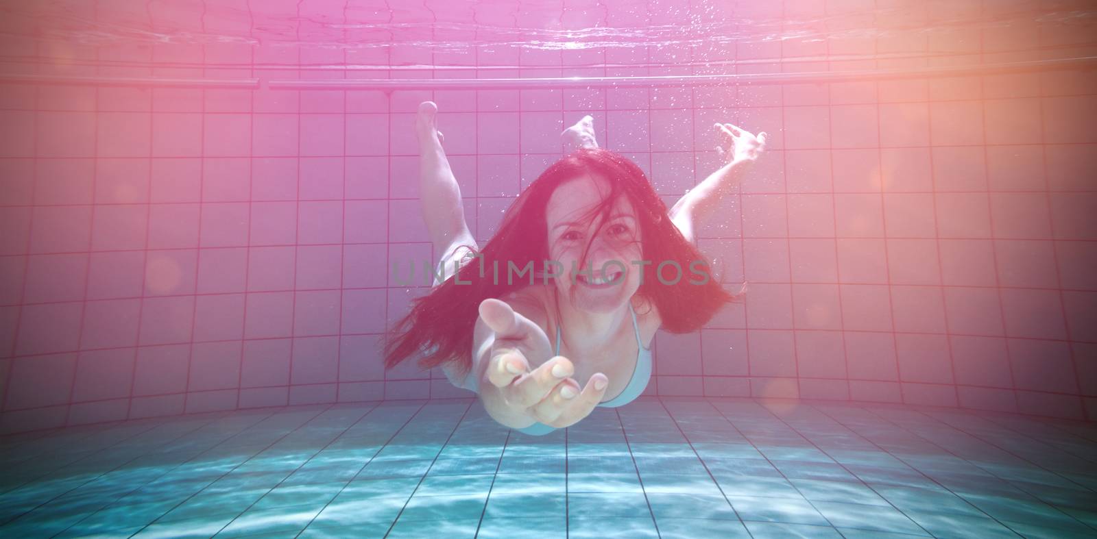 Pretty brunette smiling and offering her hand underwater in the swimming pool at the leisure centre