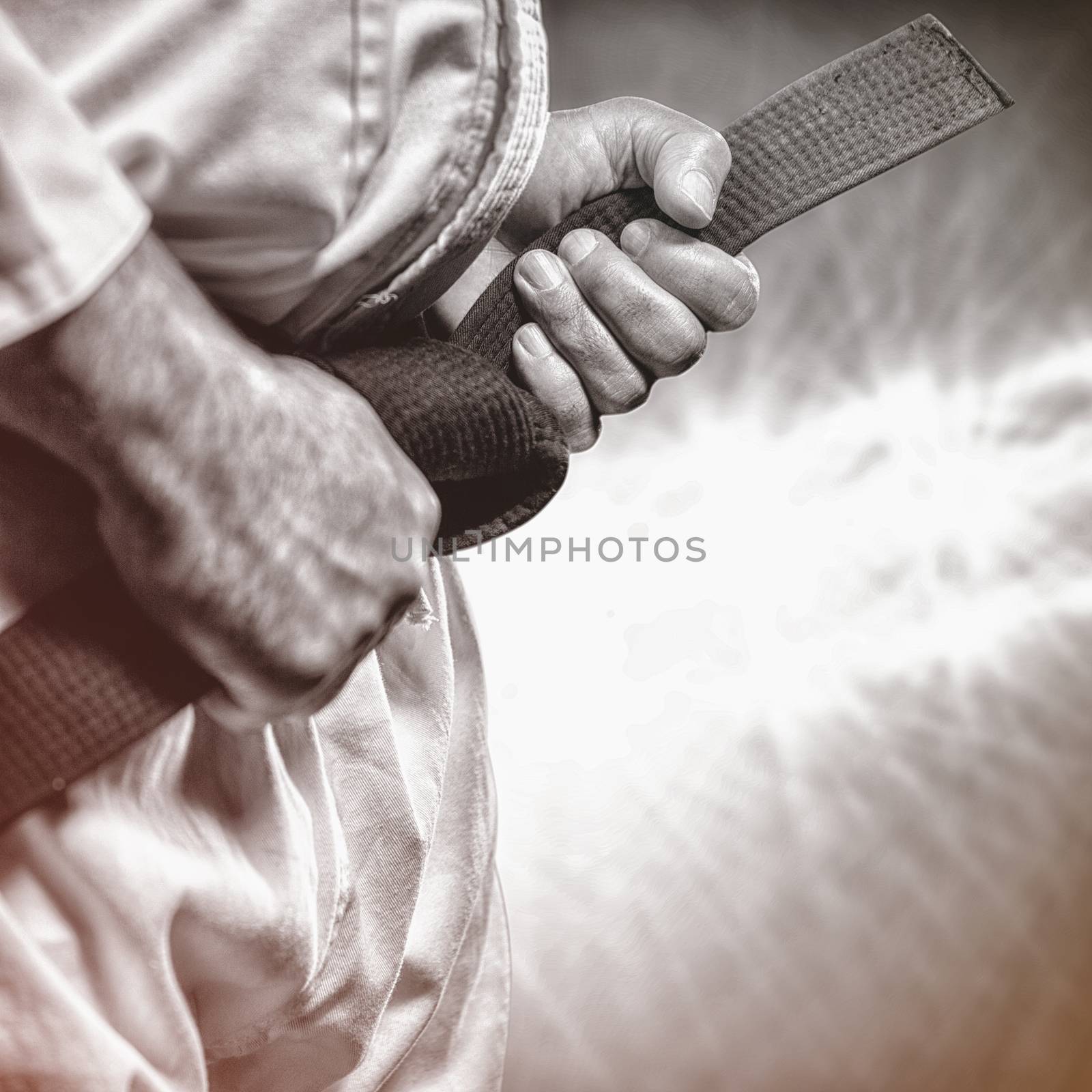 Fighter tightening karate belt against spotlights