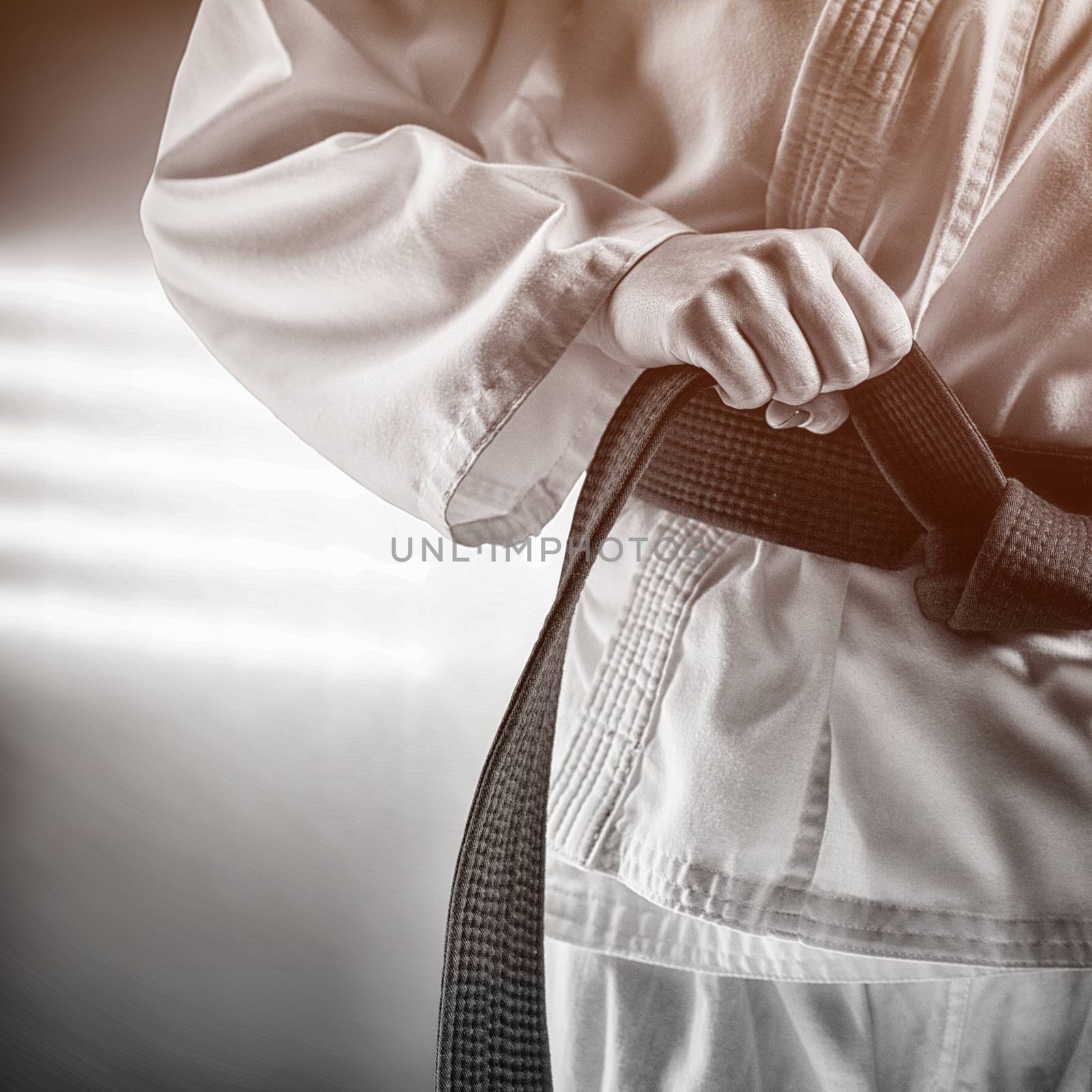Fighter tightening karate belt against spotlights
