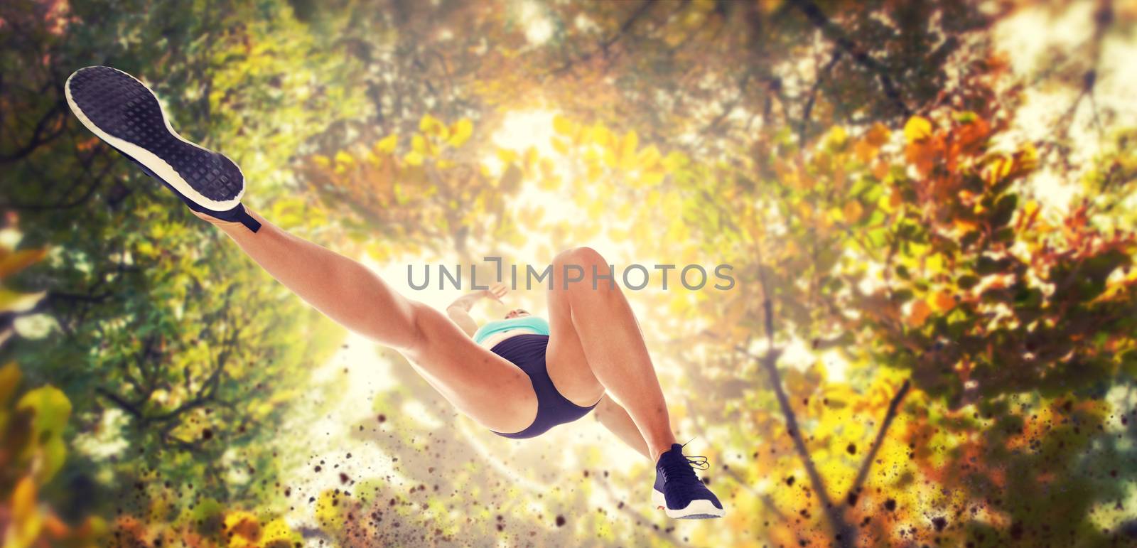 Low angle female athlete jumping against branches and autumnal leaves against the sunlight