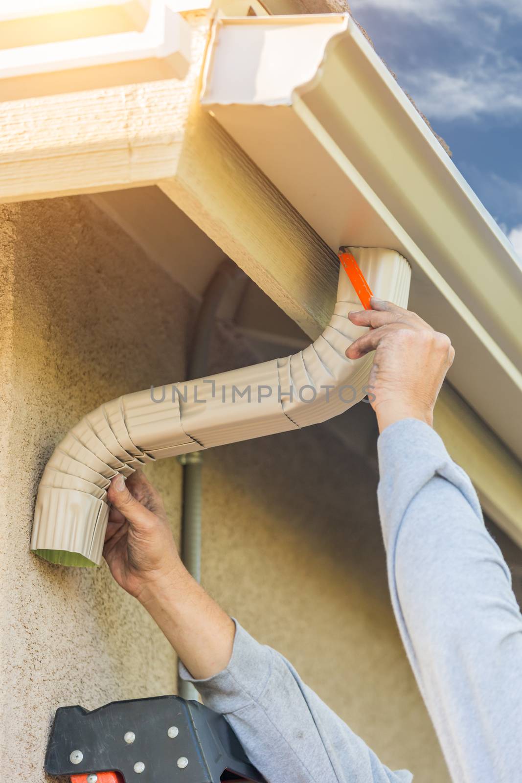 Worker Attaching Aluminum Rain Gutter and Down Spout to Fascia of House.