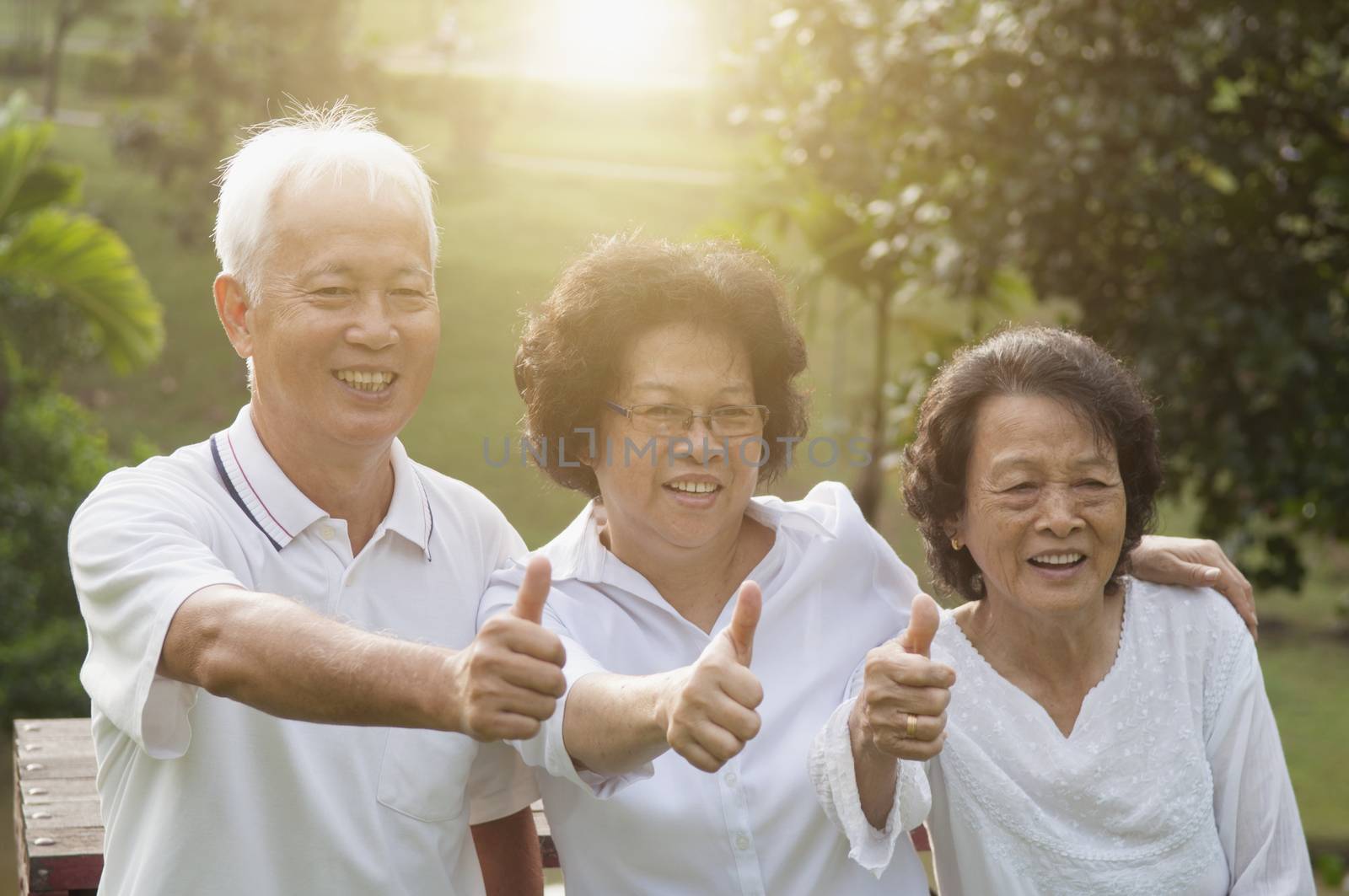 Group of cheerful Asian seniors retiree giving thumbs up at outdoor nature park, in morning beautiful sunlight at background.