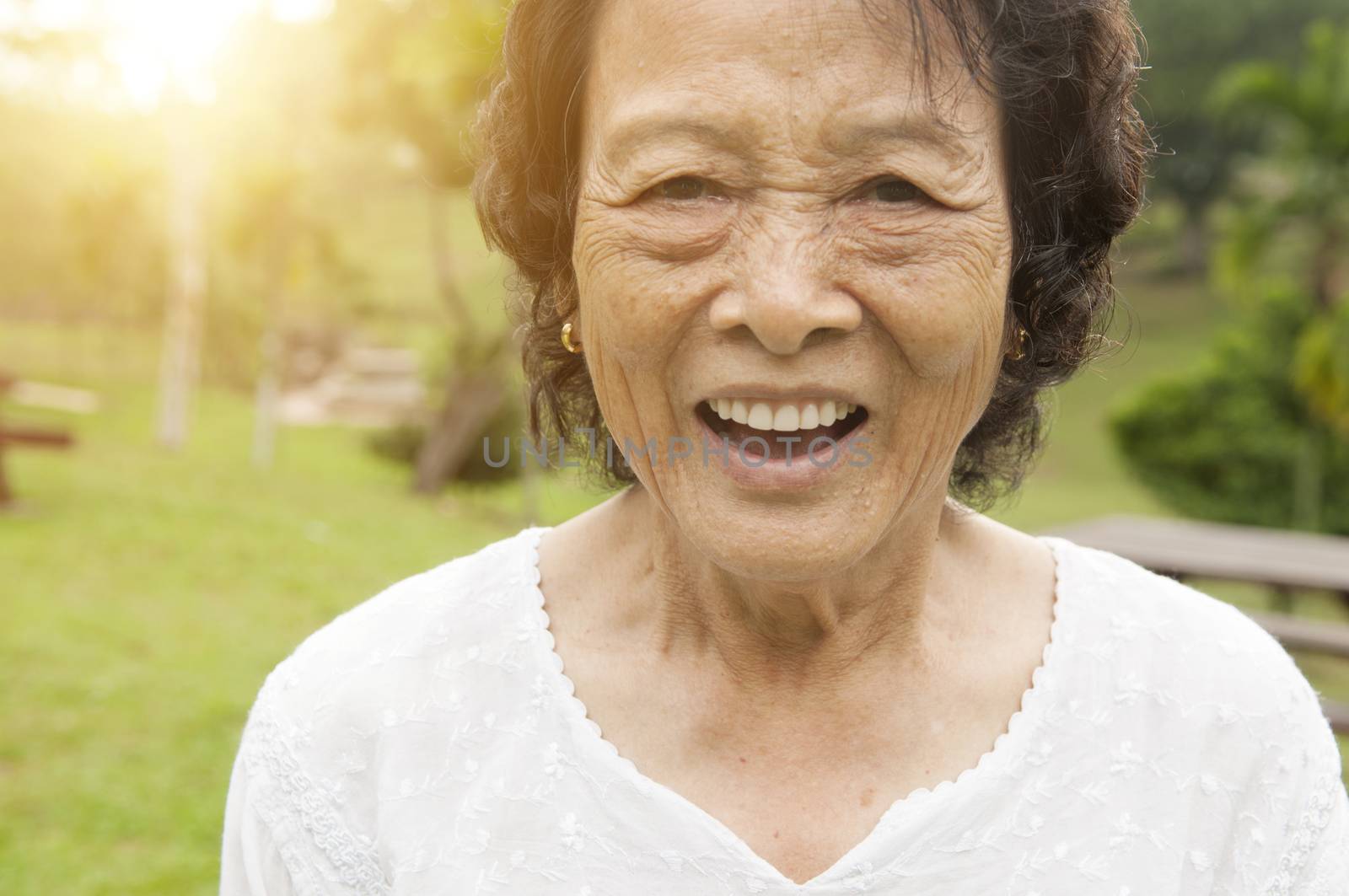 Portrait of healthy happy Asian senior woman laughing at outdoor nature park, morning beautiful sunlight background.