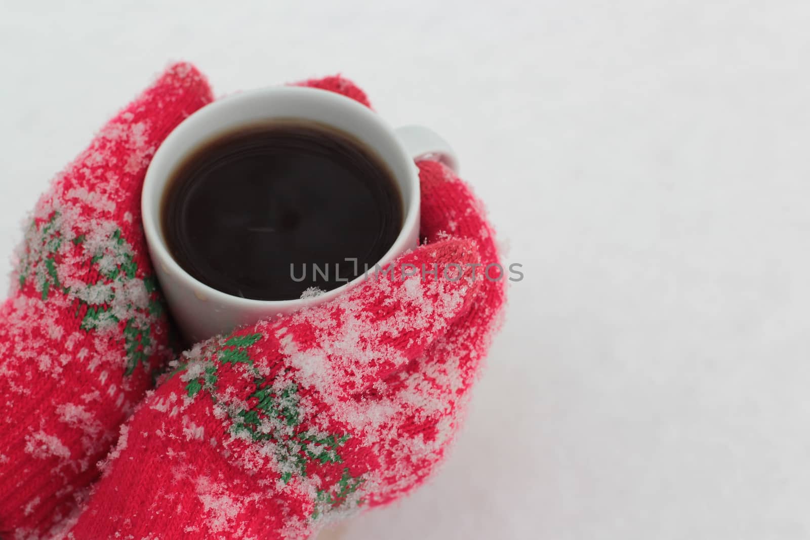 hands keep a cup of coffee against the background of snow in red gloves