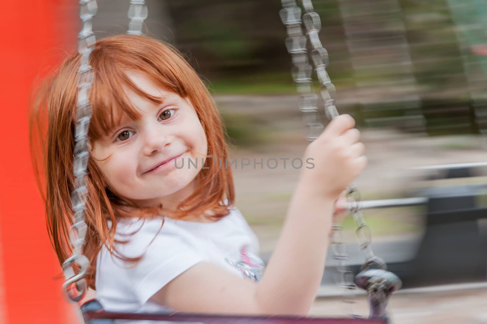 little girl with red hair smiles and playing on the swing in an amusement park, blurred background