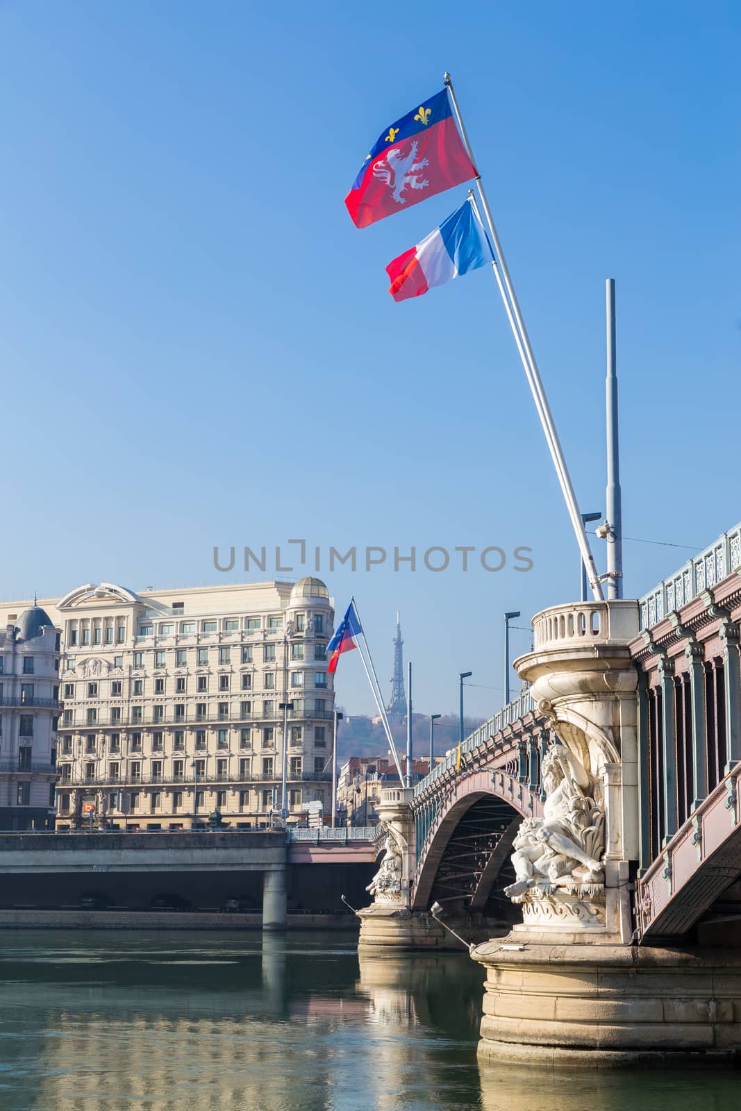 A bridge over a river with city buildings at the other side and a french flag flying