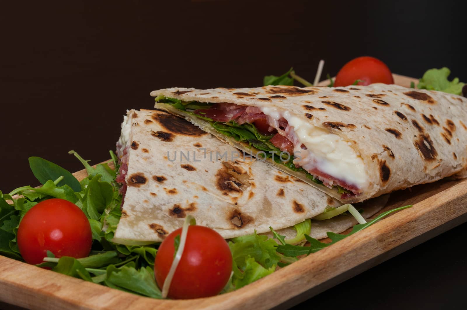 italian piadina, with salad, ham, cheese, mozzarella and tomatoes, wood dish and black background