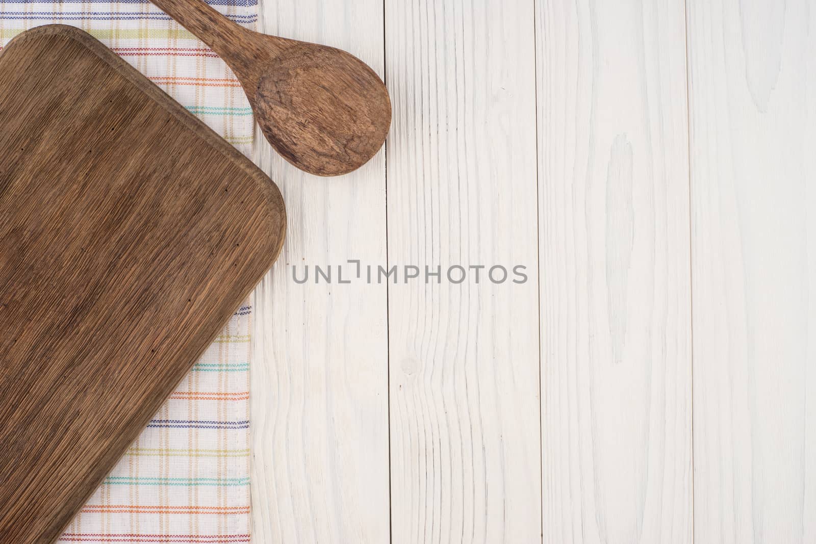 Cutting board and a spoon on a kitchen napkin on old wooden table. Top view.