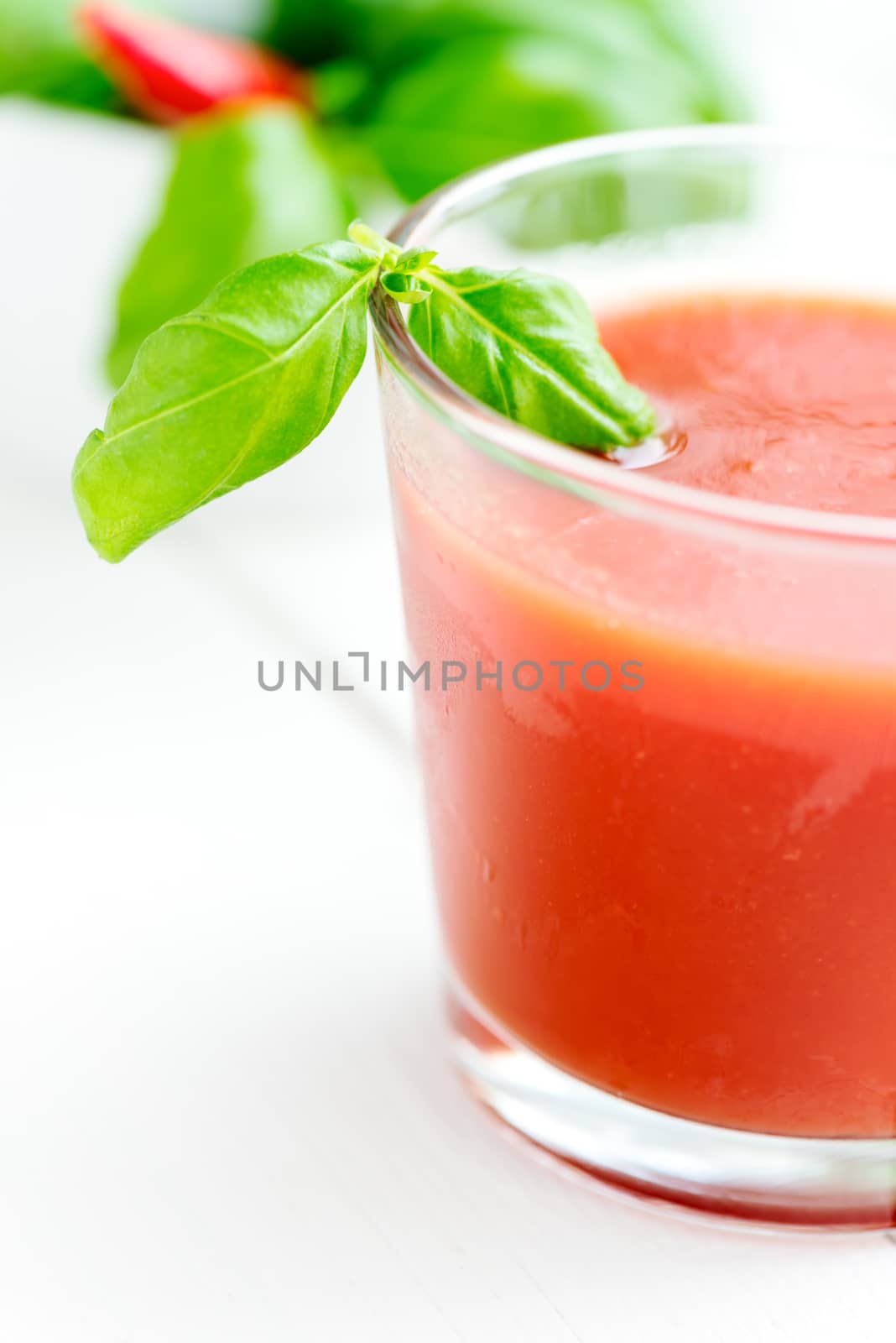 Cold tomato juice in a glass with basil leafs close up