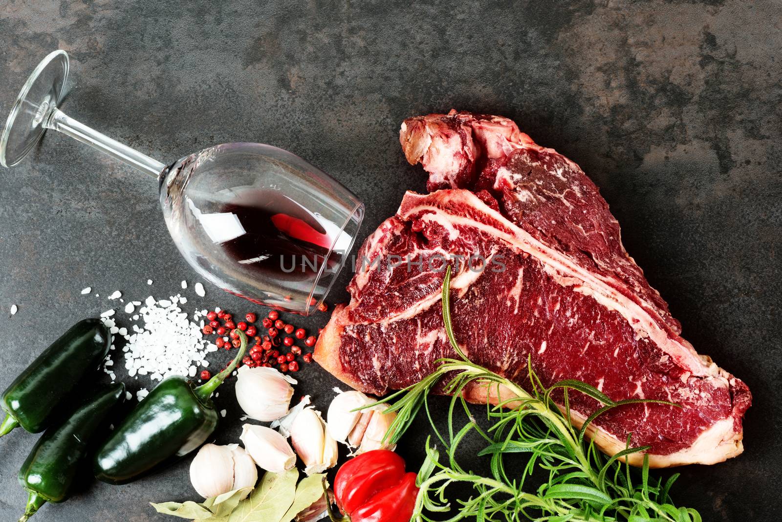 Raw aged meat T-bone steak and seasoning on dark background