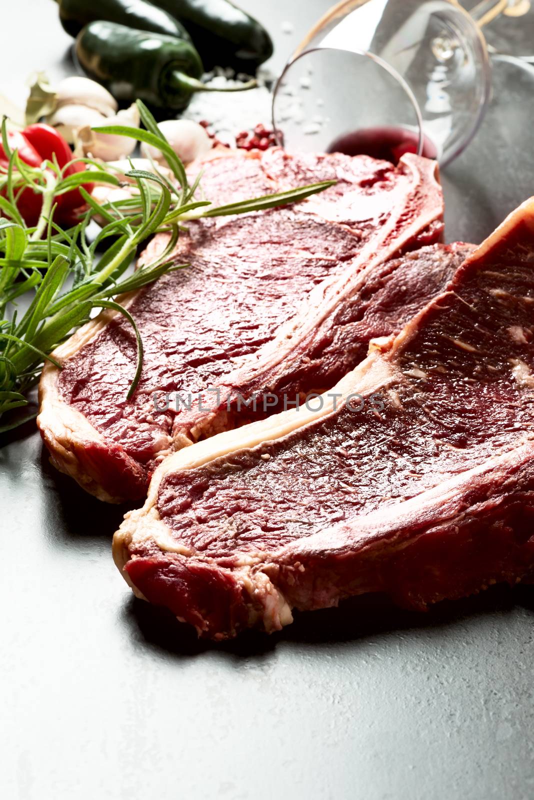 Raw aged meat T-bone steak and seasoning on dark background