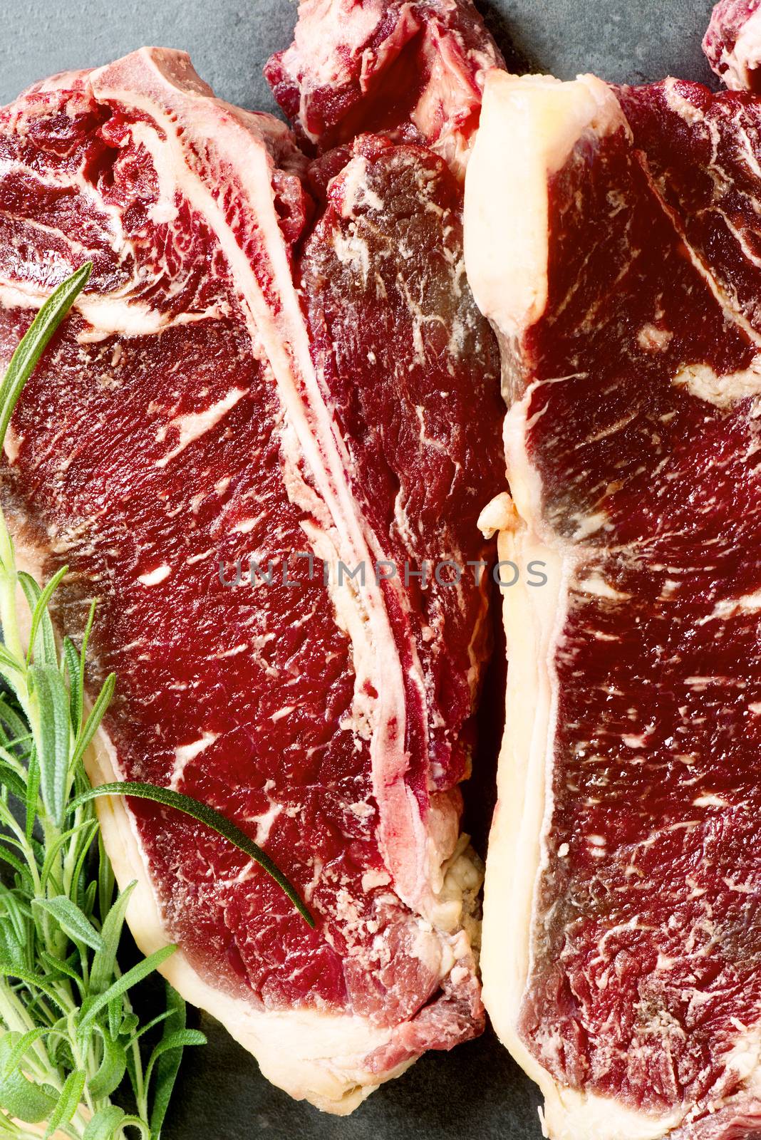 Raw aged meat T-bone steak and seasoning on dark background