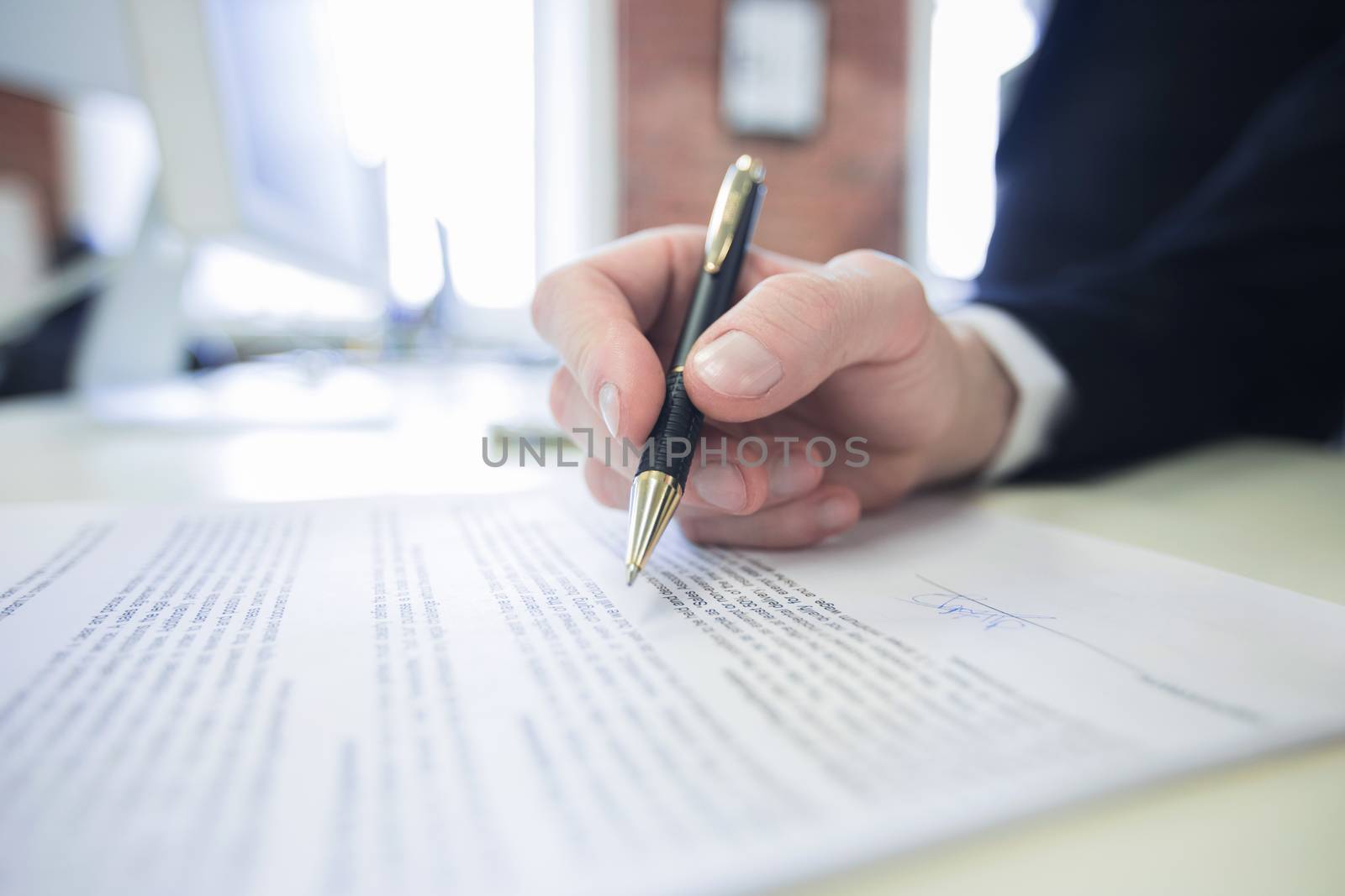 Businessman sitting at office desk signing a contract with shallow focus on signature and pen