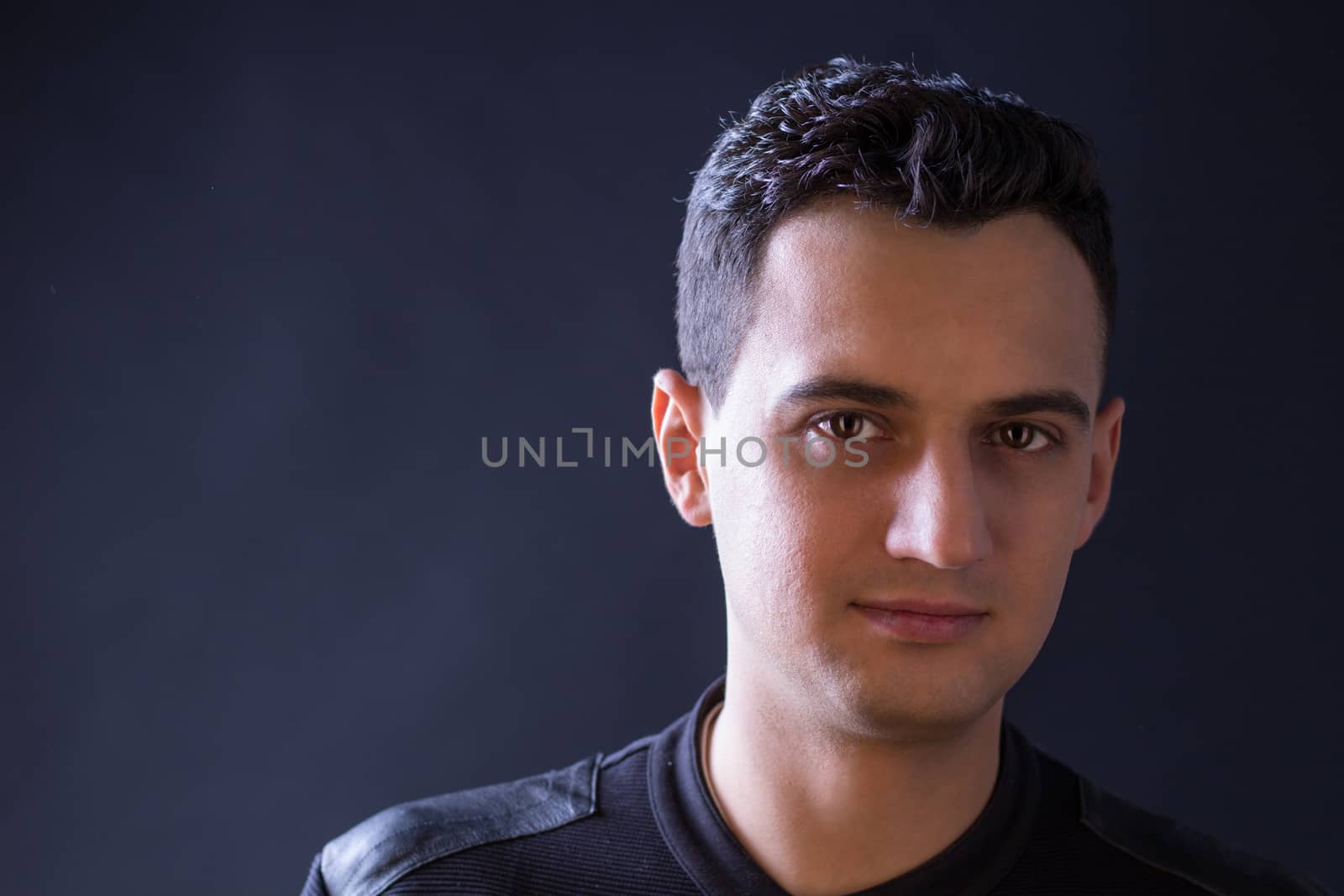 Close-up portrait of black-haired man lightened by projector on black background