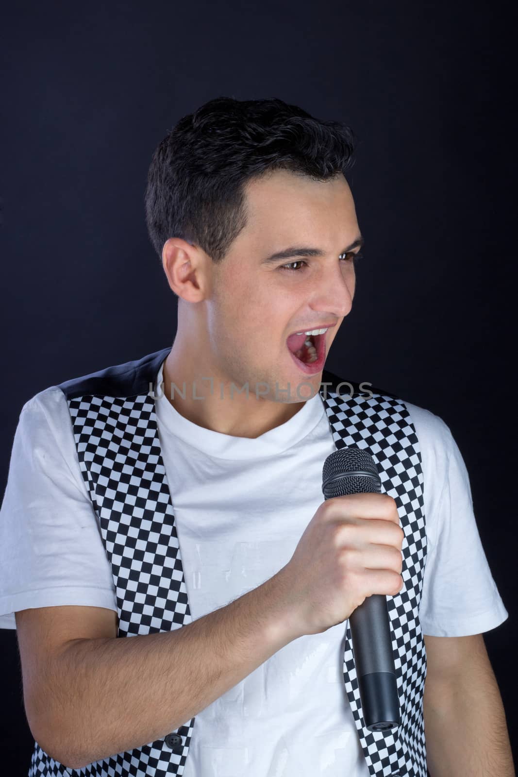 Young black-haired man dressed in black and white performs singing to microphone