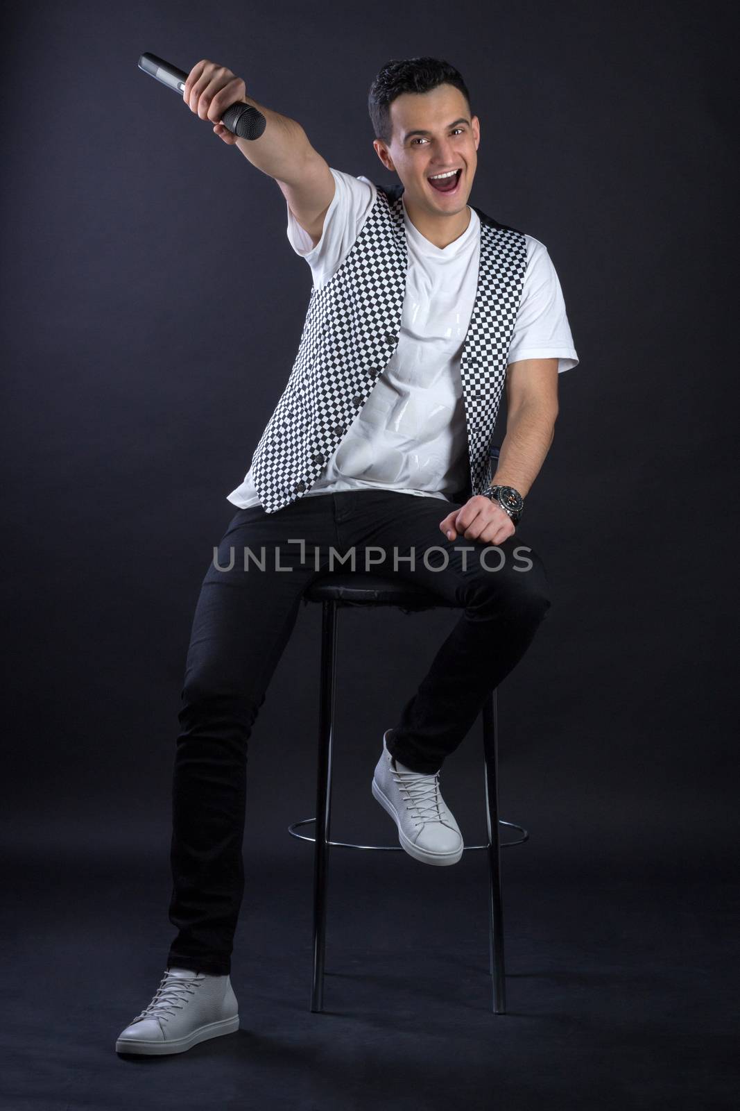 Young black-haired man dressed in black and white poses singing to microphone