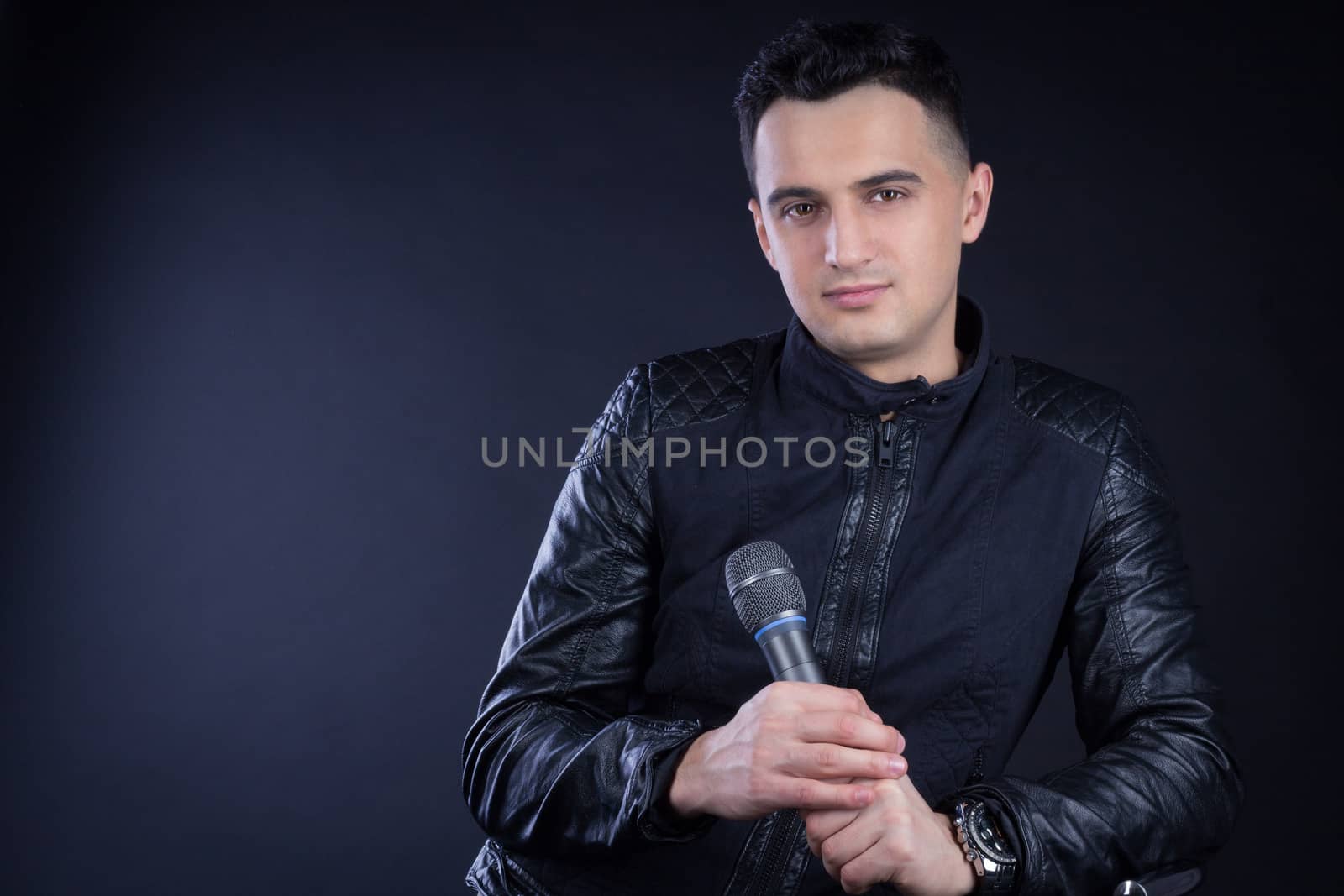 Young black-haired man dressed in black and white poses singing to microphone