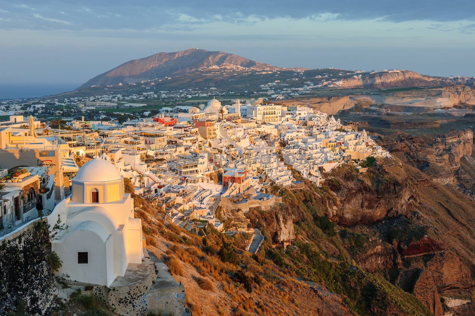 Fira, Santorini island, Greece - April 2016: Illuminated Luxury balcony decks and patios with restaurants of Fira town at Santorini island, in warm rays of sunset. Santorini is one of most famous greek resorts situated in Aegean sea at old volcano's caldera.