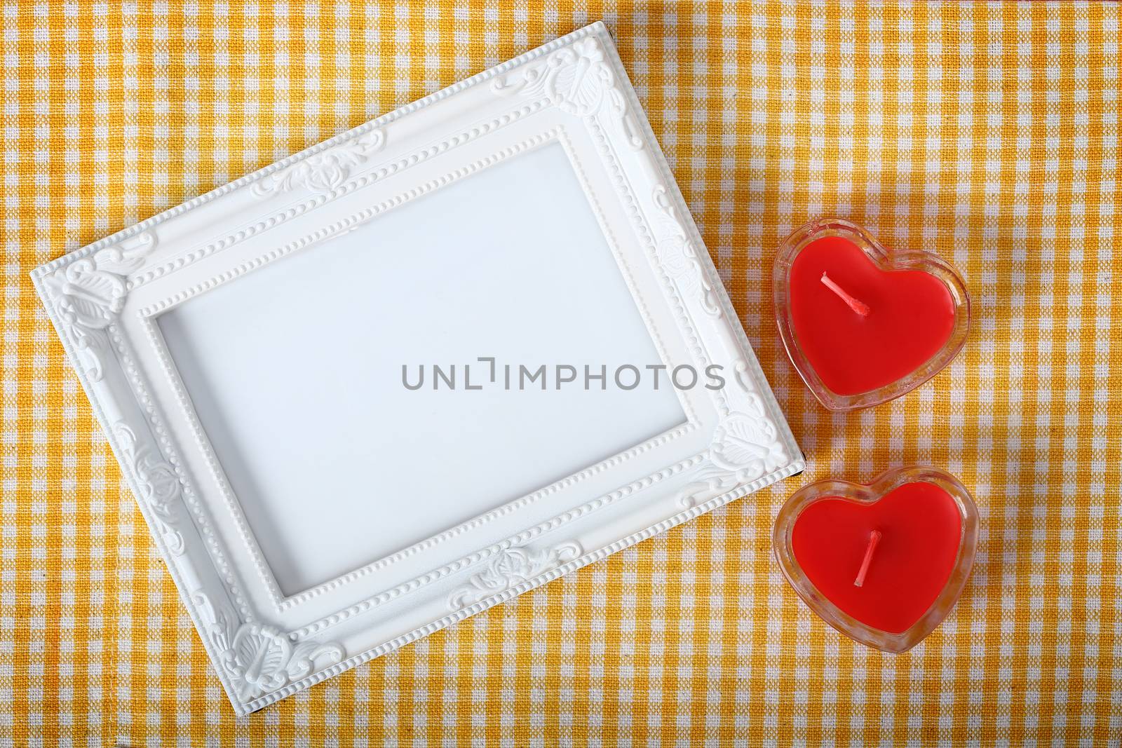 Top view of empty white photo frame next heart sign from candle over the yellow fabric, clipping path ready to put photographs.