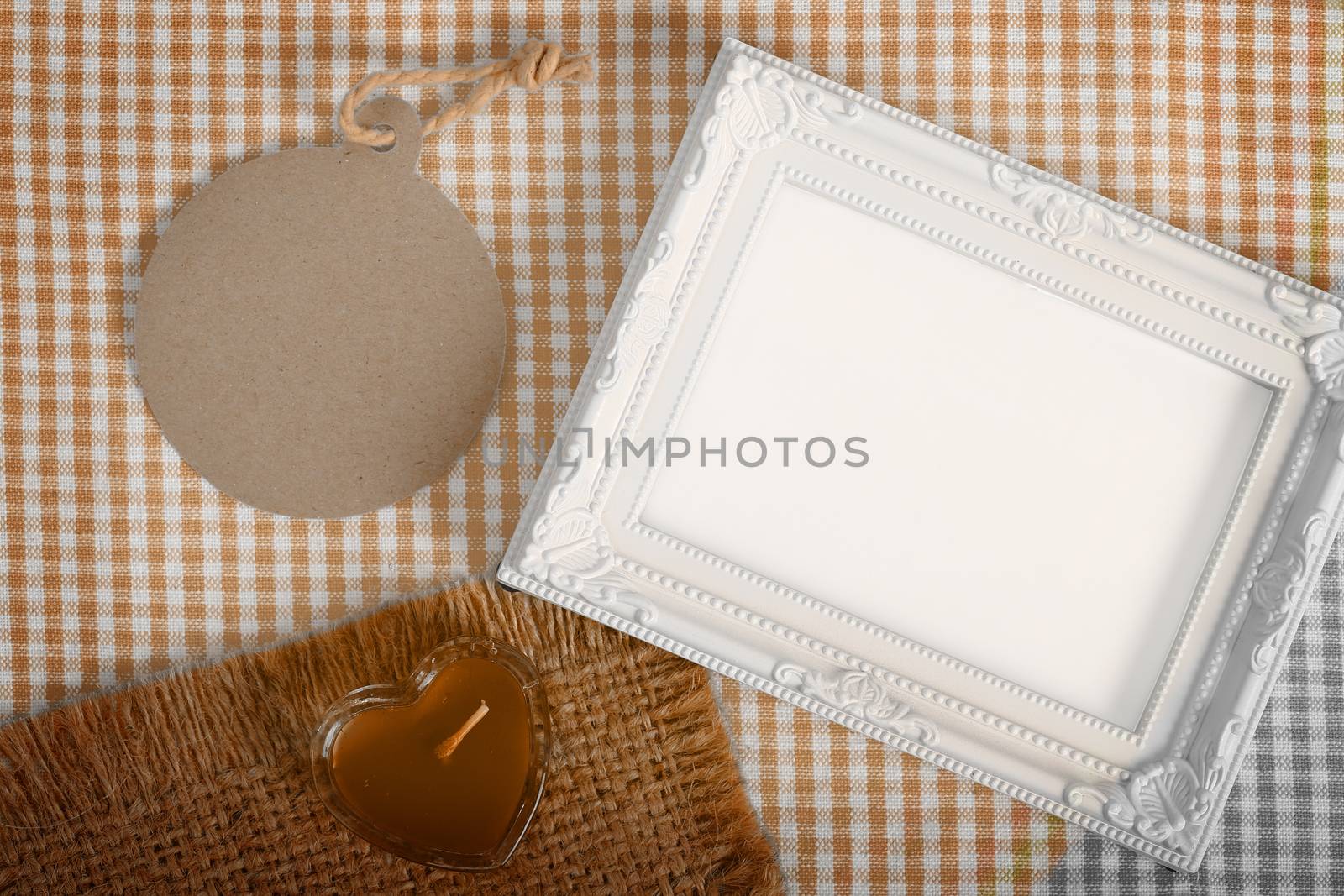 Top view of empty white photo frame and paper tag next heart sign from candle in glass over the fabric, clipping path ready to put photographs.