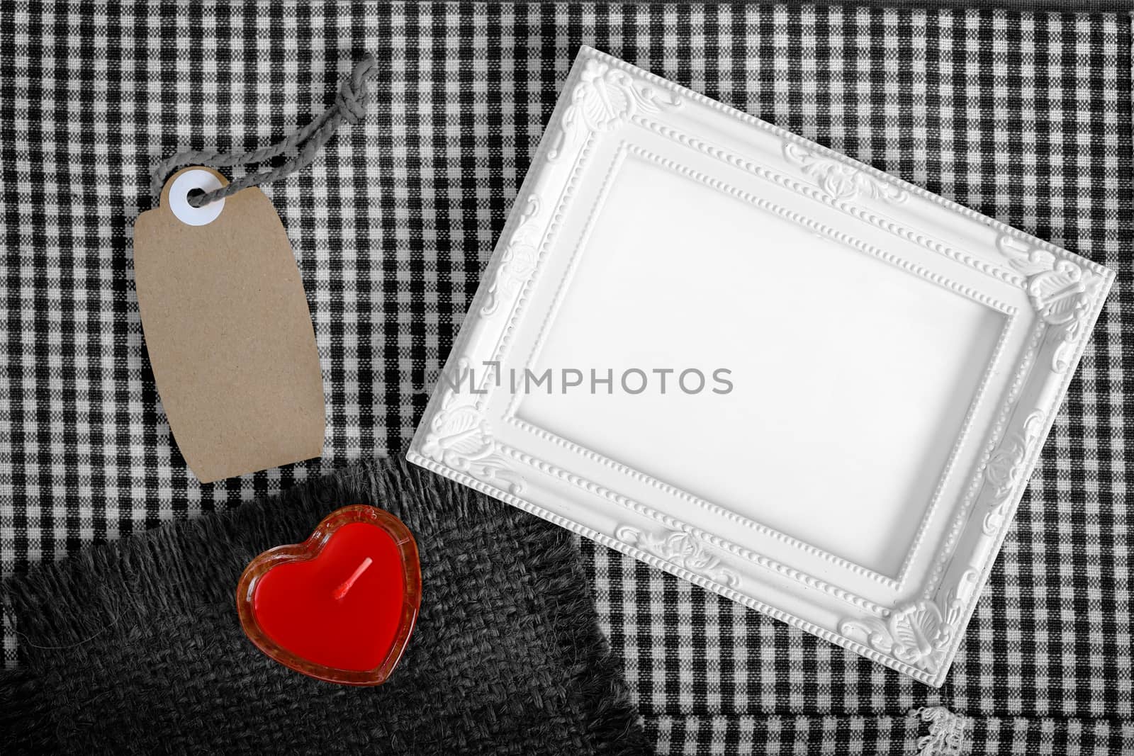 Top view of empty white photo frame next red heart sign from candle and paper tag, clipping path ready to put photographs.