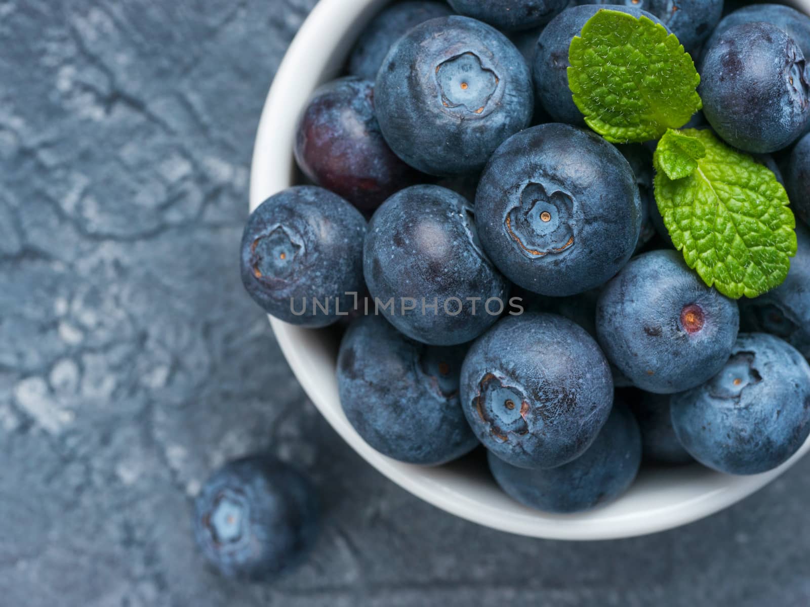 Freshly picked blueberries closeup. Ripe and juicy fresh blueberry with green mint leaves on textured concrete background. Bilberry on gray background with copyspace. Top view or flat lay