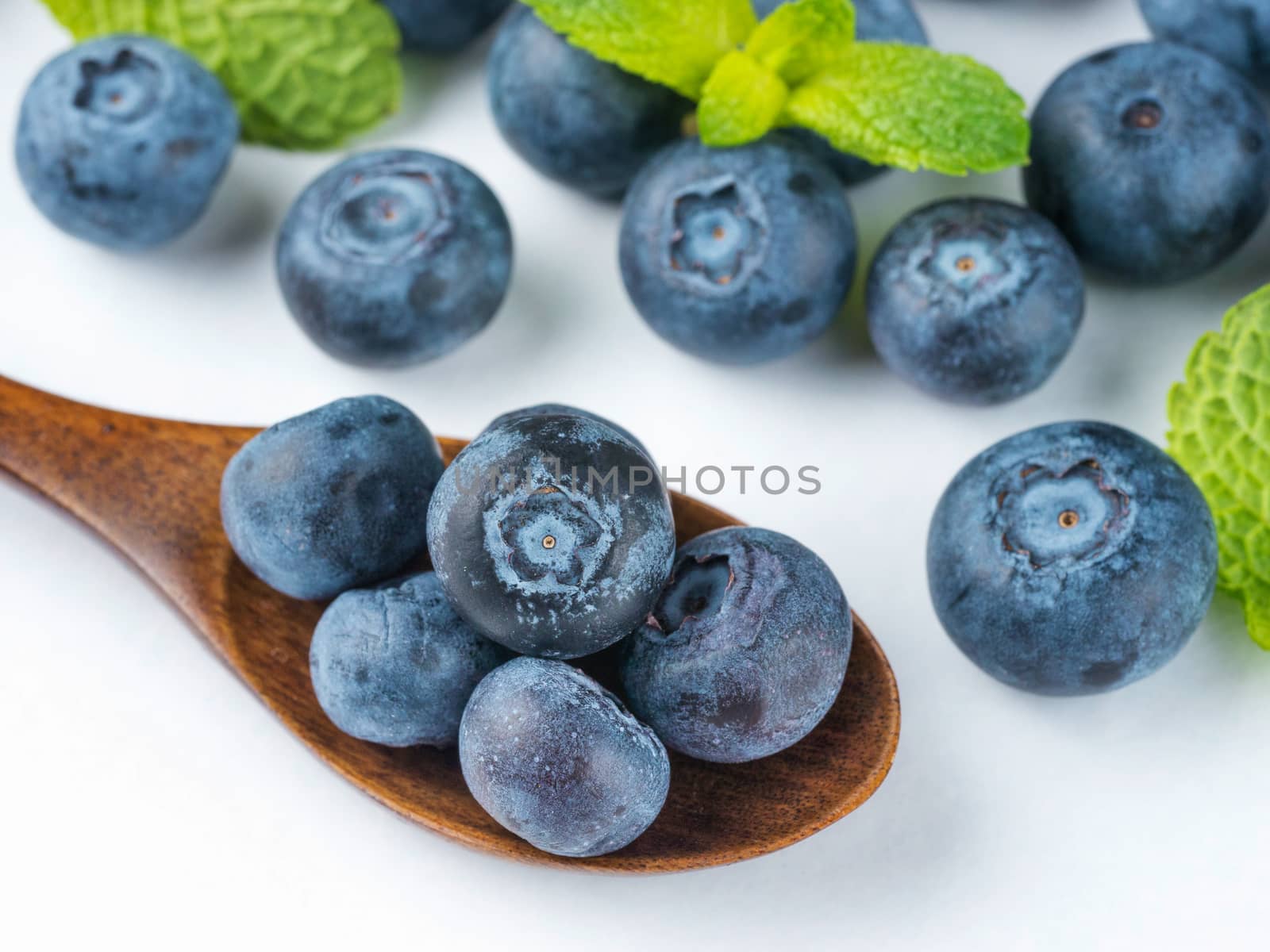 Freshly picked blueberries in wooden spoon closeup. Ripe and juicy fresh blueberries with green mint leaves on white background. Bilberry antioxidant. Healthy eating concept