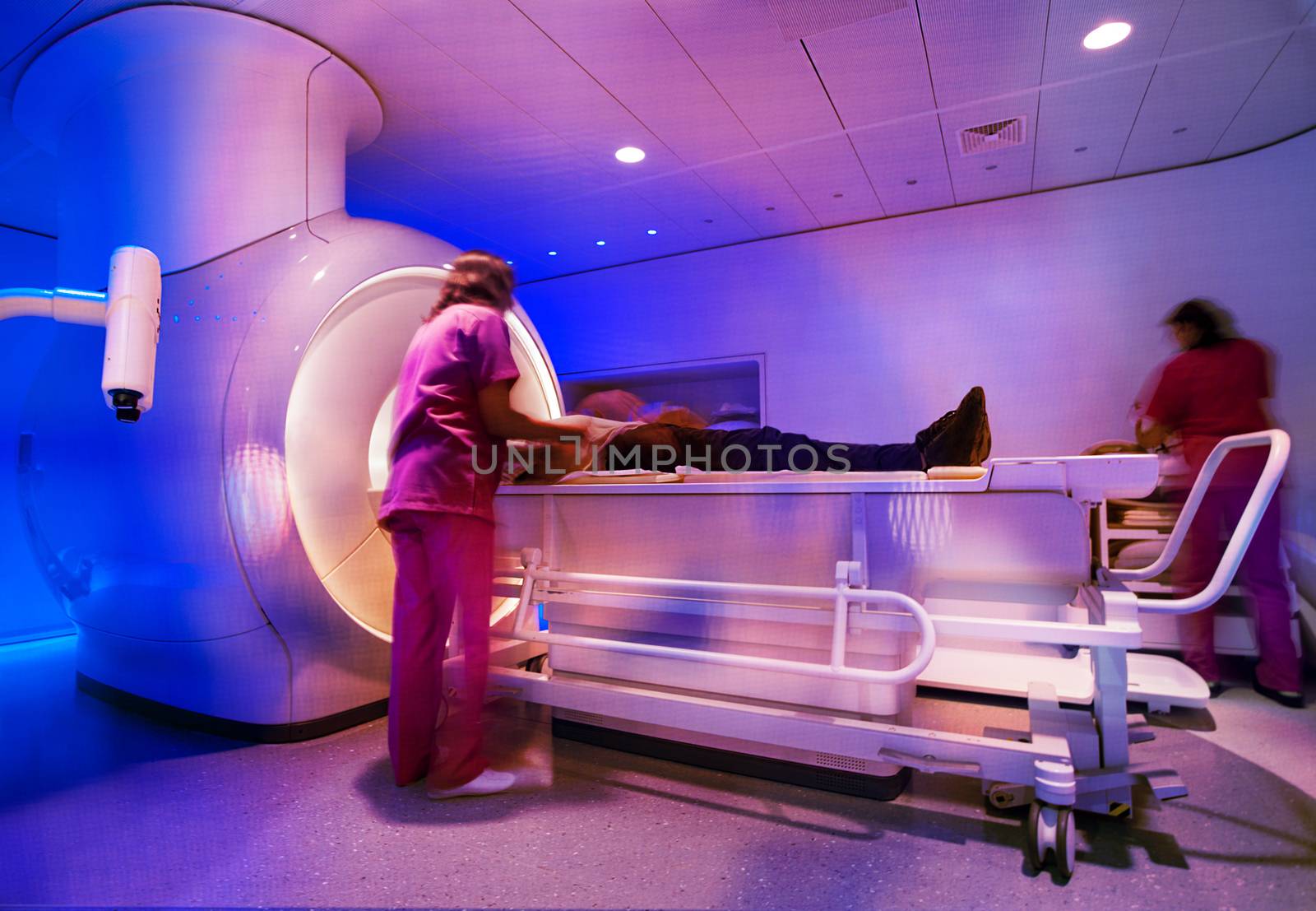 A super powerful modern magnetic resonance scanner is being prepared by nurses for scan with a patient.
