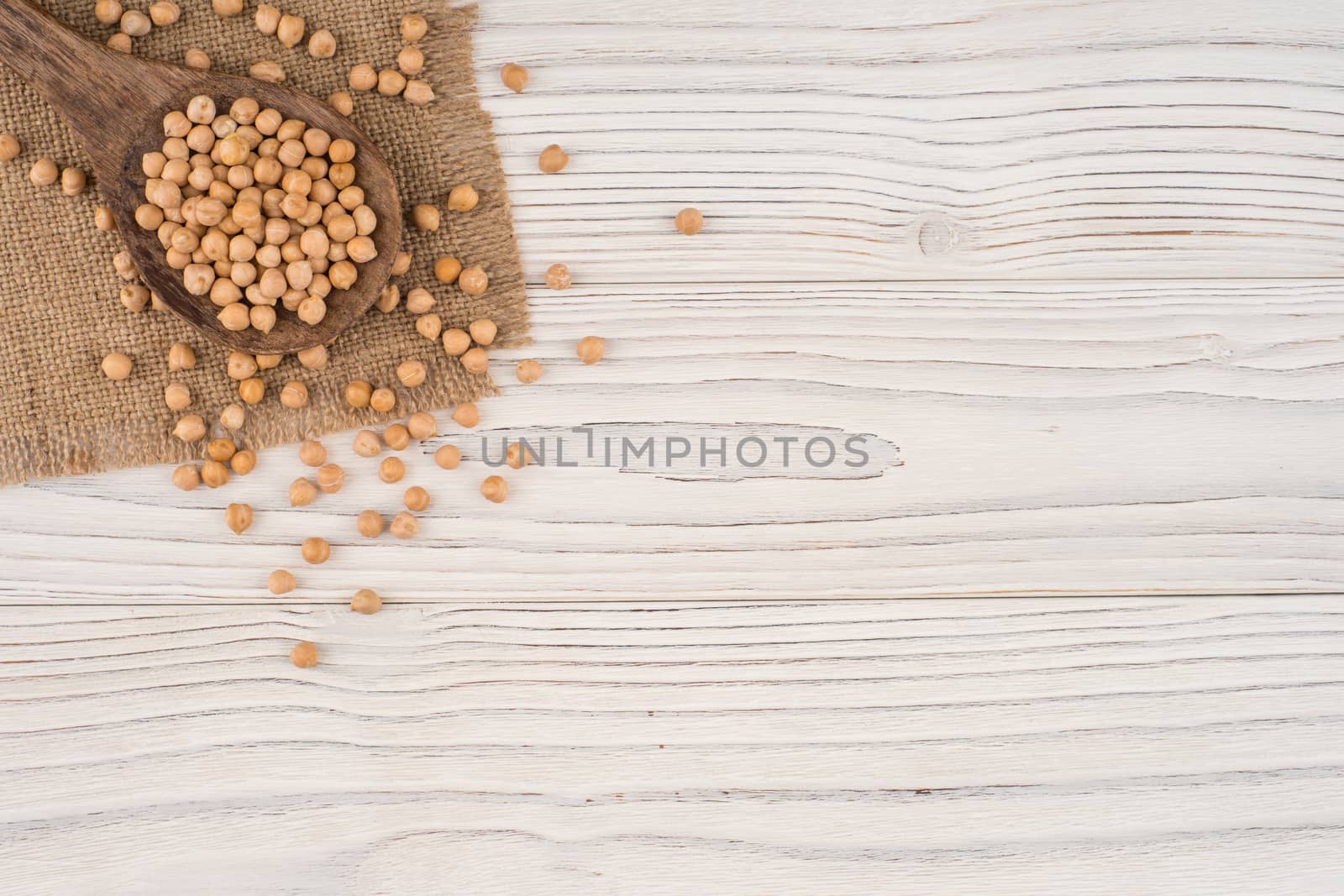 Chickpeas in a wooden spoon and an old white wooden table. Top view.