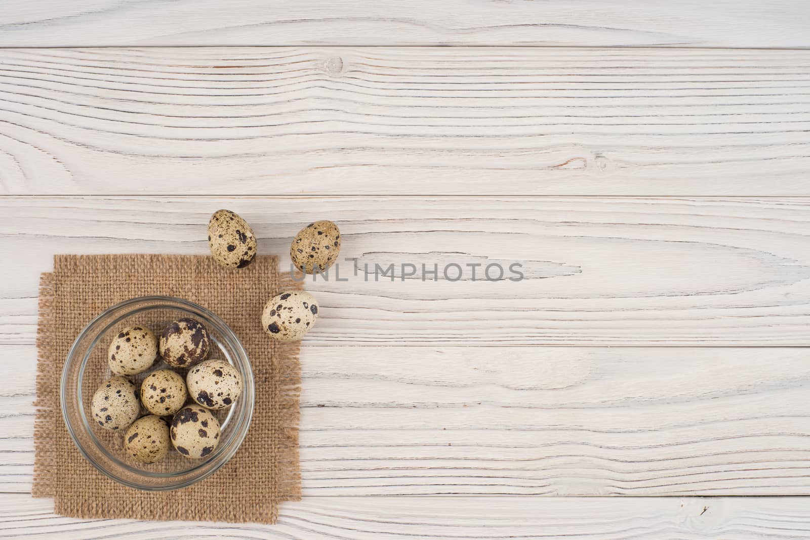 Quail eggs in a glass bowl on the old wooden table. Top view.