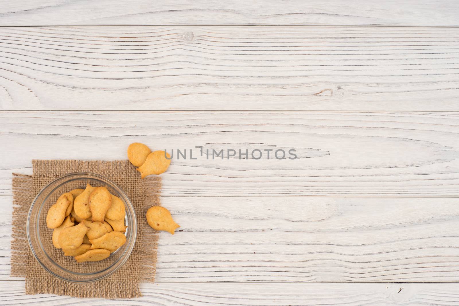 Goldfish cracker in a glass bowl on a white wooden table. Top view.