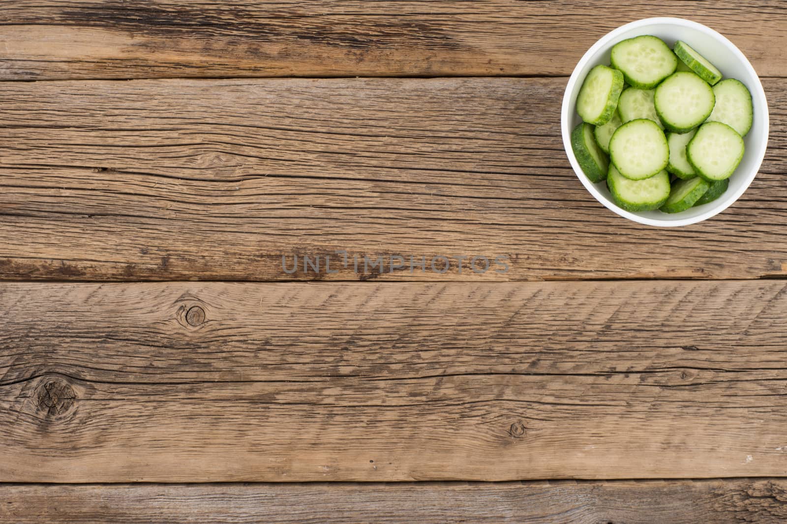 Cut cucumbers in a white bowl on old wooden table. by DGolbay