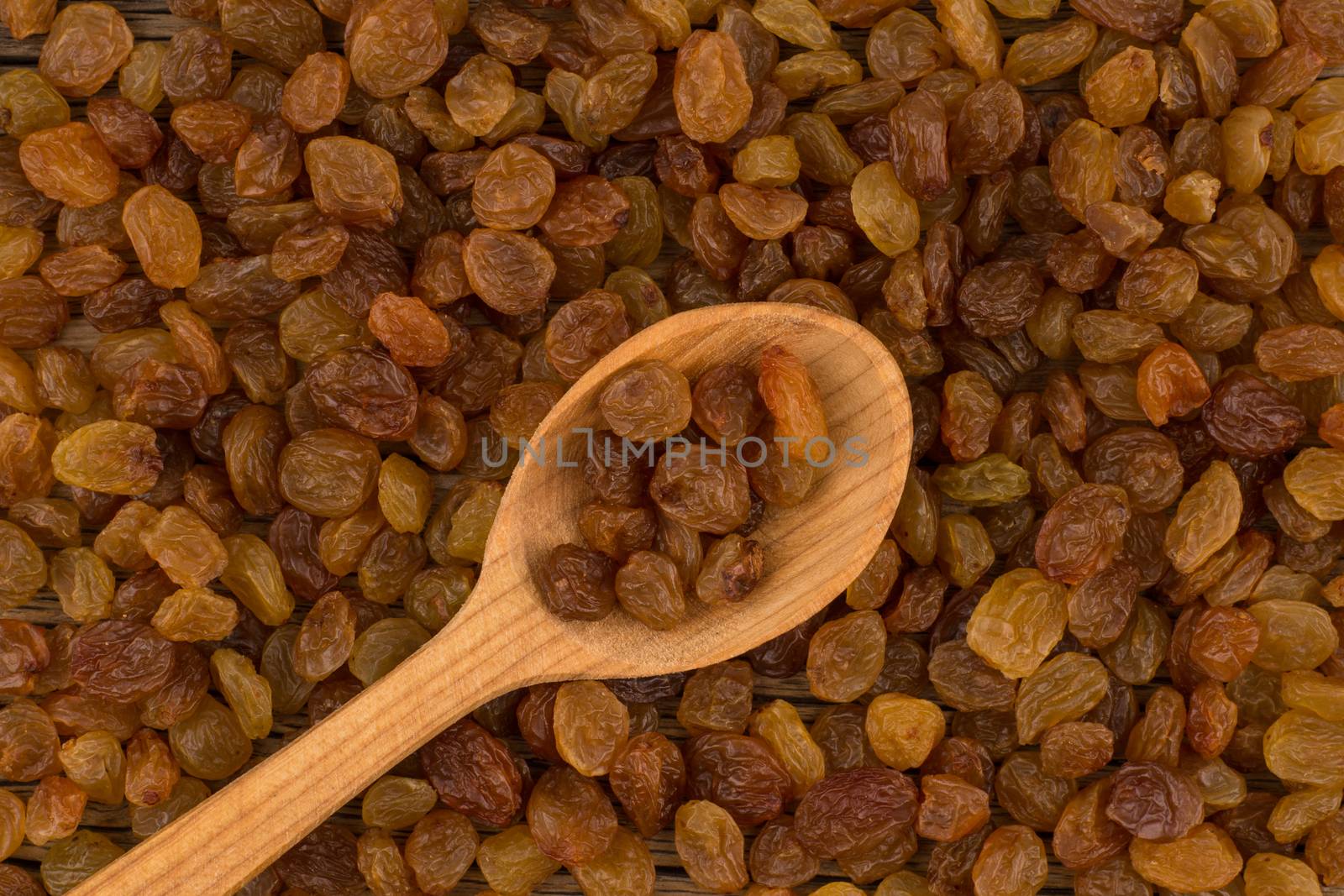Raisins in wooden spoon and background of raisins. by DGolbay