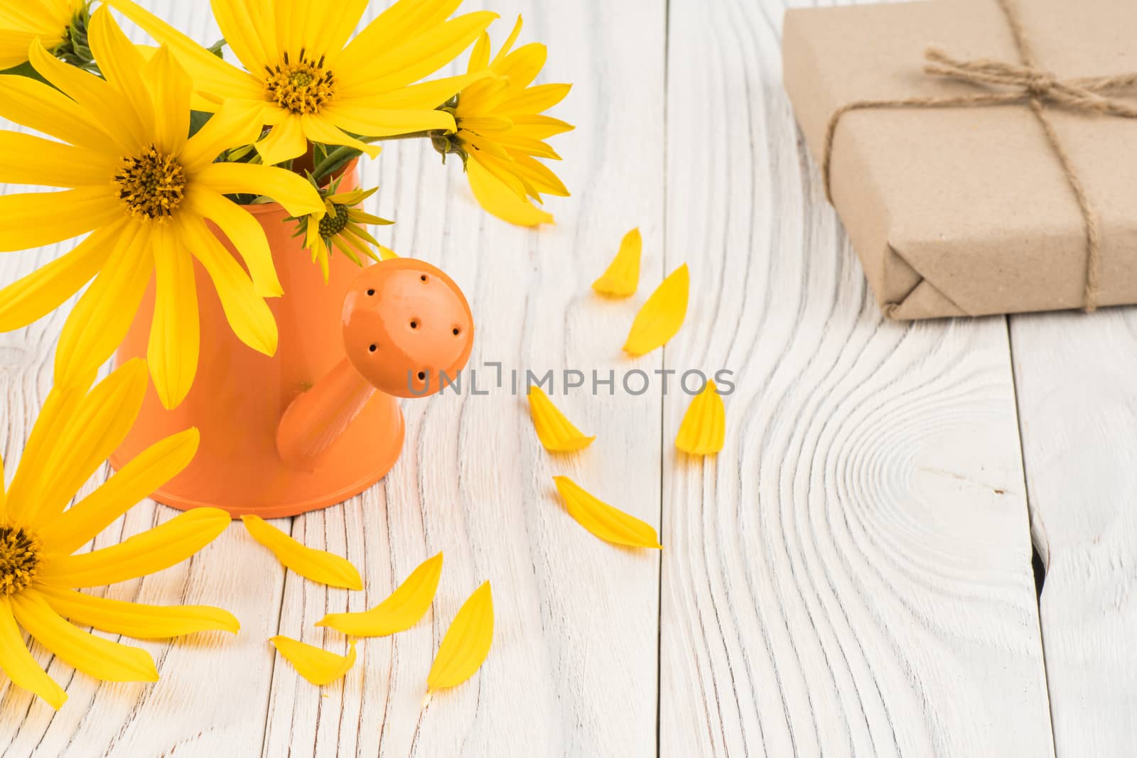 Wild flowers in a watering can with a gift box on a wooden table by DGolbay