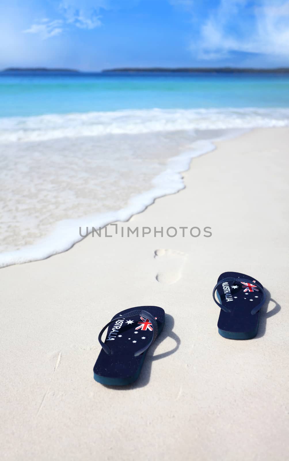 Australian flag thongs on the beach with footprints leading into the ocean.  Holiday, vacation, travel, leisure, unwind