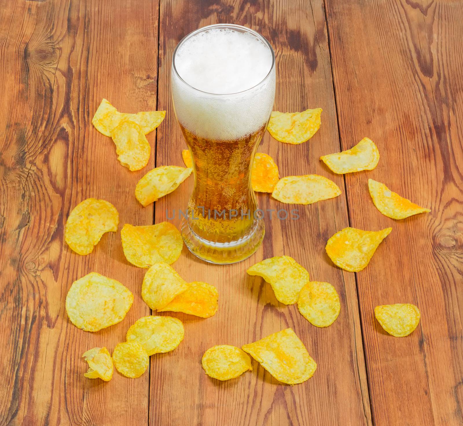 Lager beer among potato chips scattered on the wooden surface by anmbph