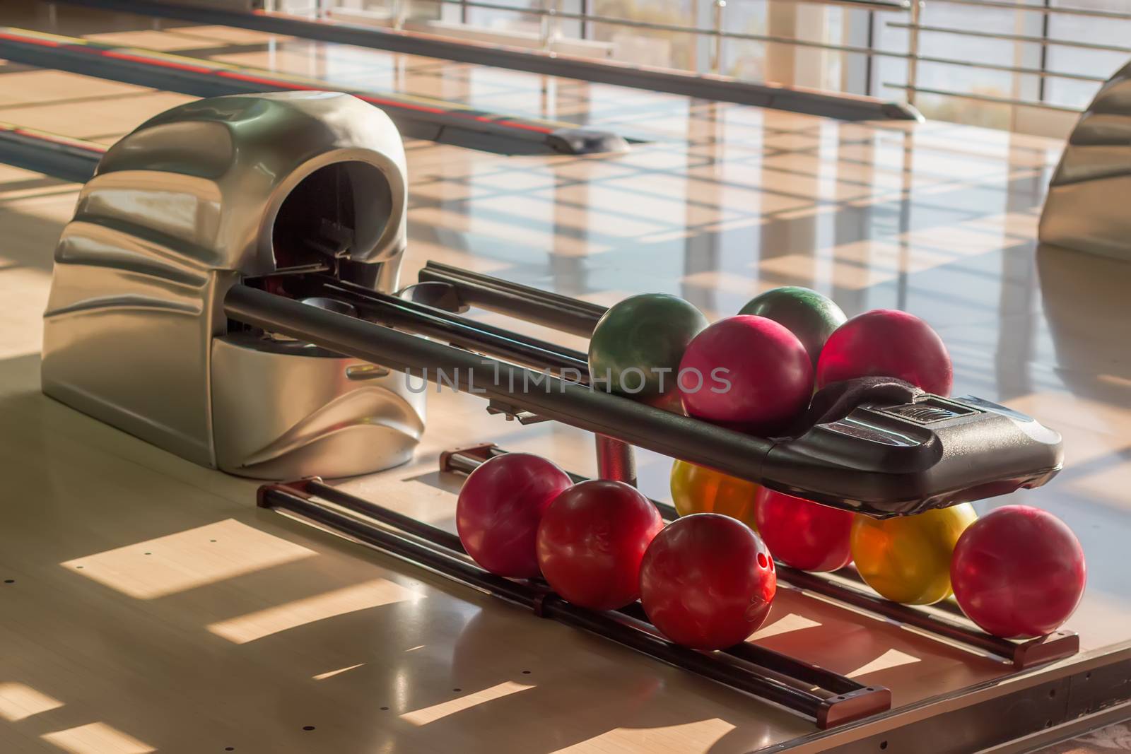 Colored bowling balls with a three finger holes on the ball return device in a modern pin bowling alley
