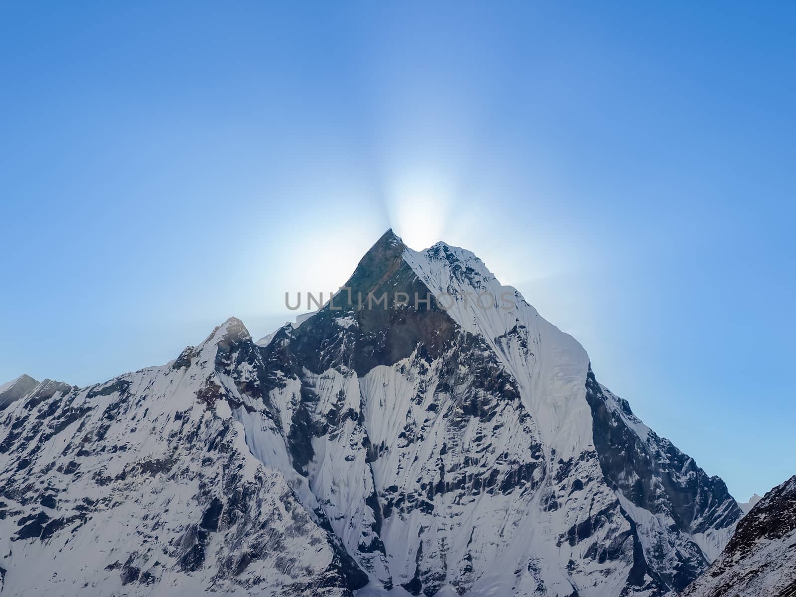 Mountain peak covered glaciers and rays of rising sun from behind him against the background of the sky early morning in the Himalayas
