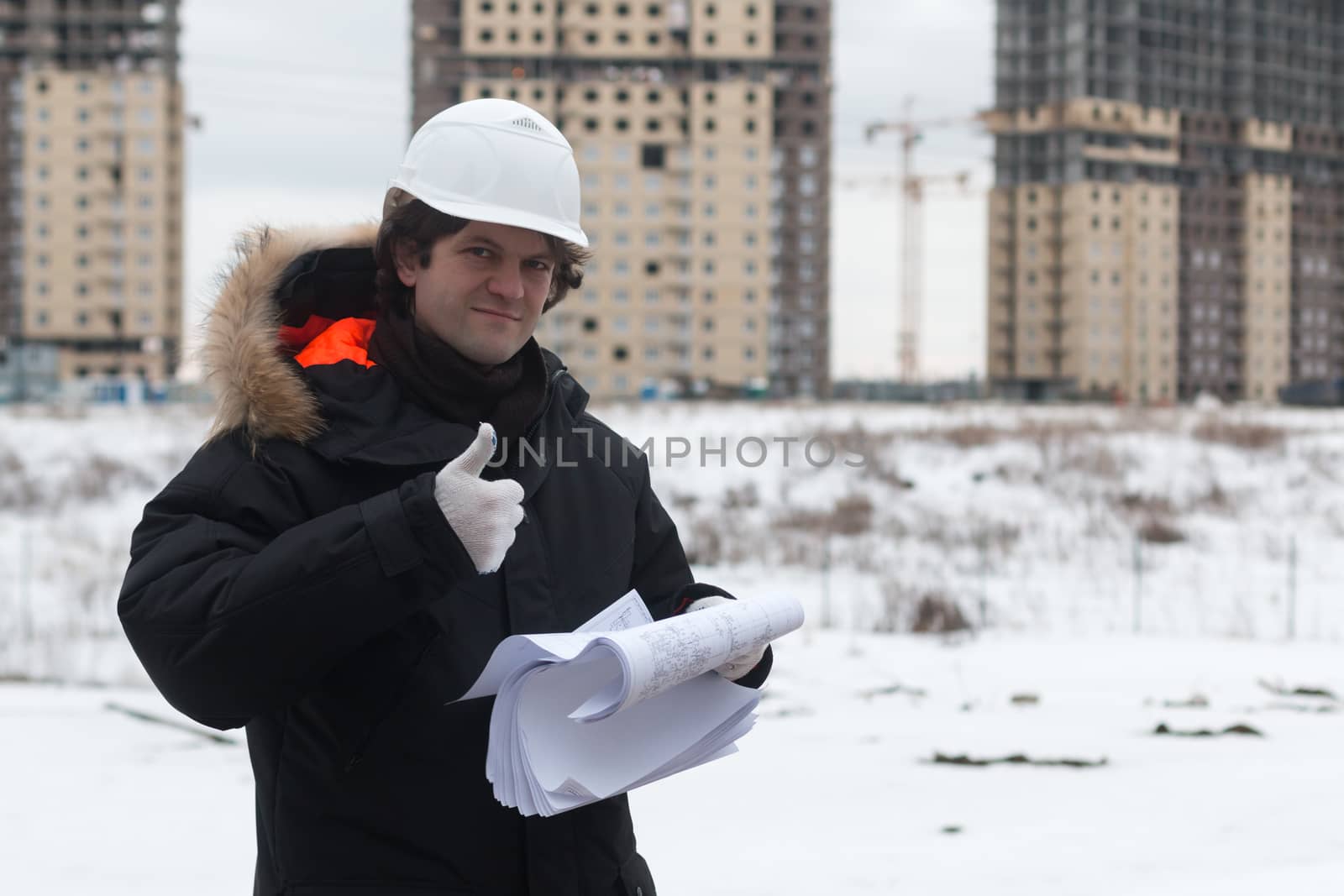 Engineer standing on the background of a new apartment building. House is built. Engineer in a helmet with papers in hand on the phone. The concept of new housing construction, real estate.