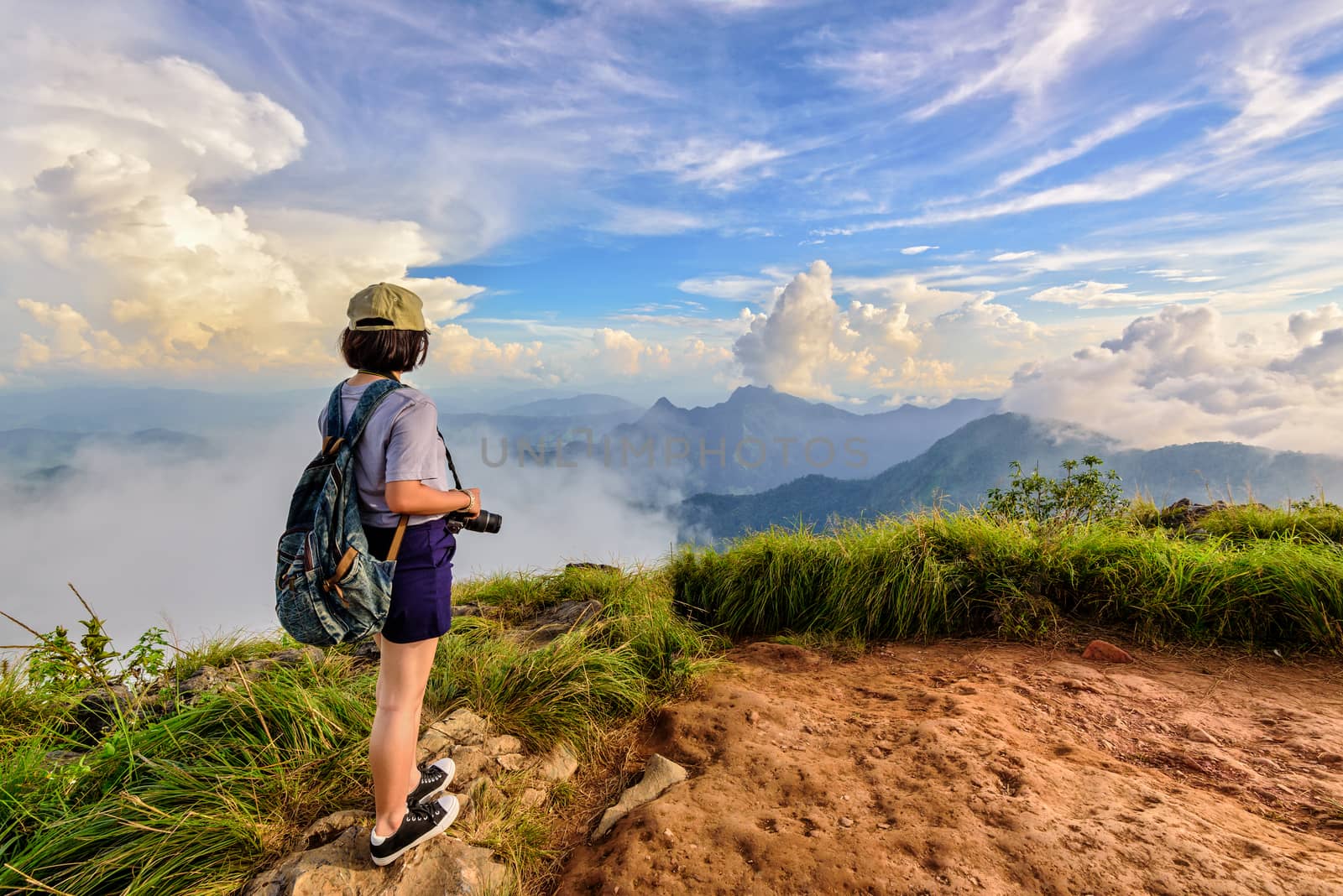 Hiker asian teens girl with camera and backpack wear caps and glasses looking beautiful landscape nature of mountain range and blue sky during sunset at Phu Chi Fa Forest Park, Chiang Rai, Thailand